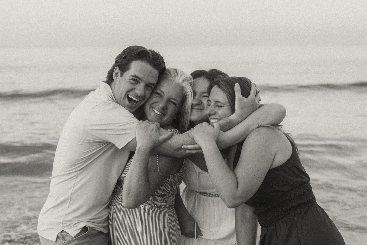 A couple embraces and laughs together on a beach during a black and white photoshoot.