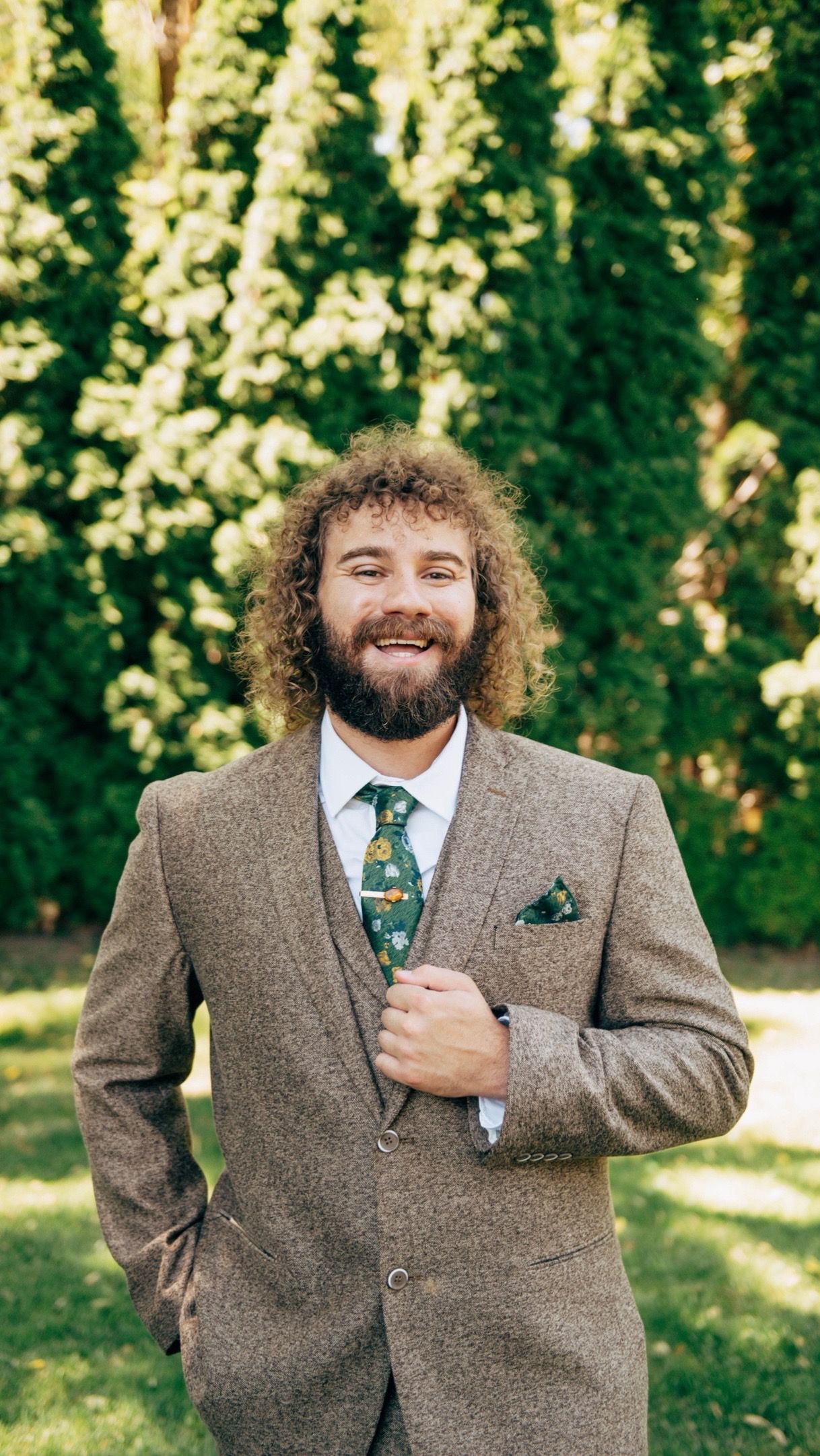 Bearded groom in tweed suit and green tie smiling joyfully in outdoor portrait series.
