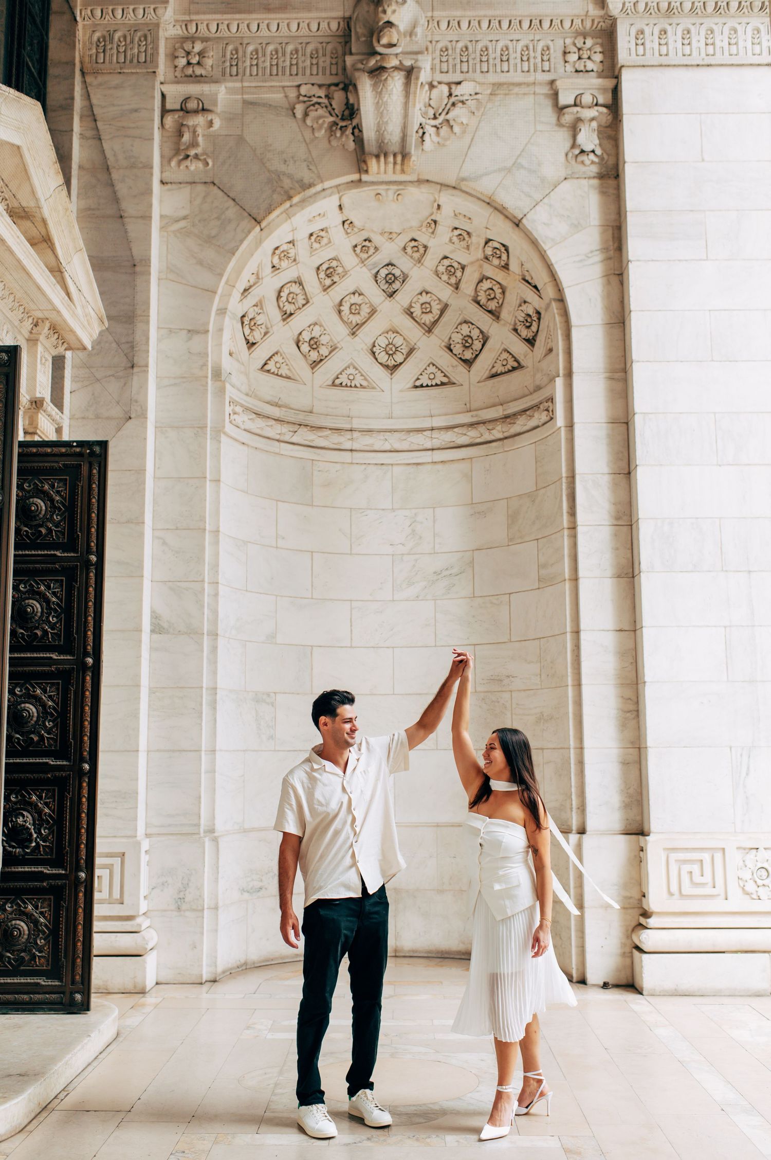 Couple dancing and holding hands in an ornate marble archway of a elegant historic building.