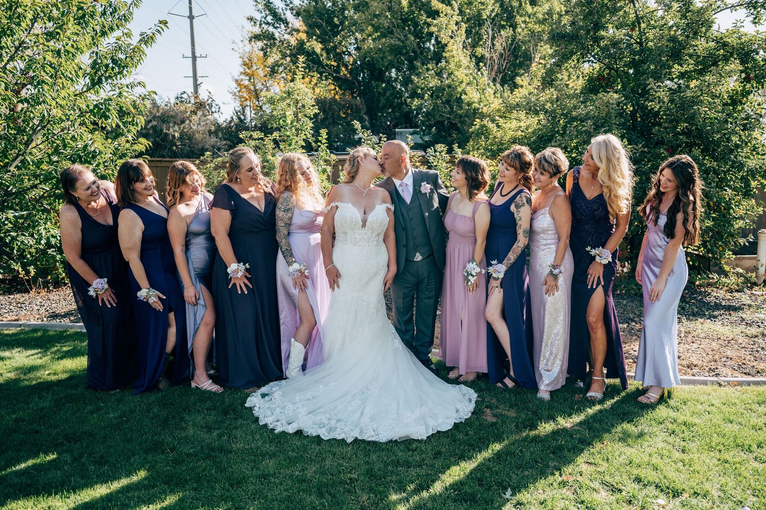 Wedding party in navy and pink dresses poses together outdoors on a sunny day with green trees in background.