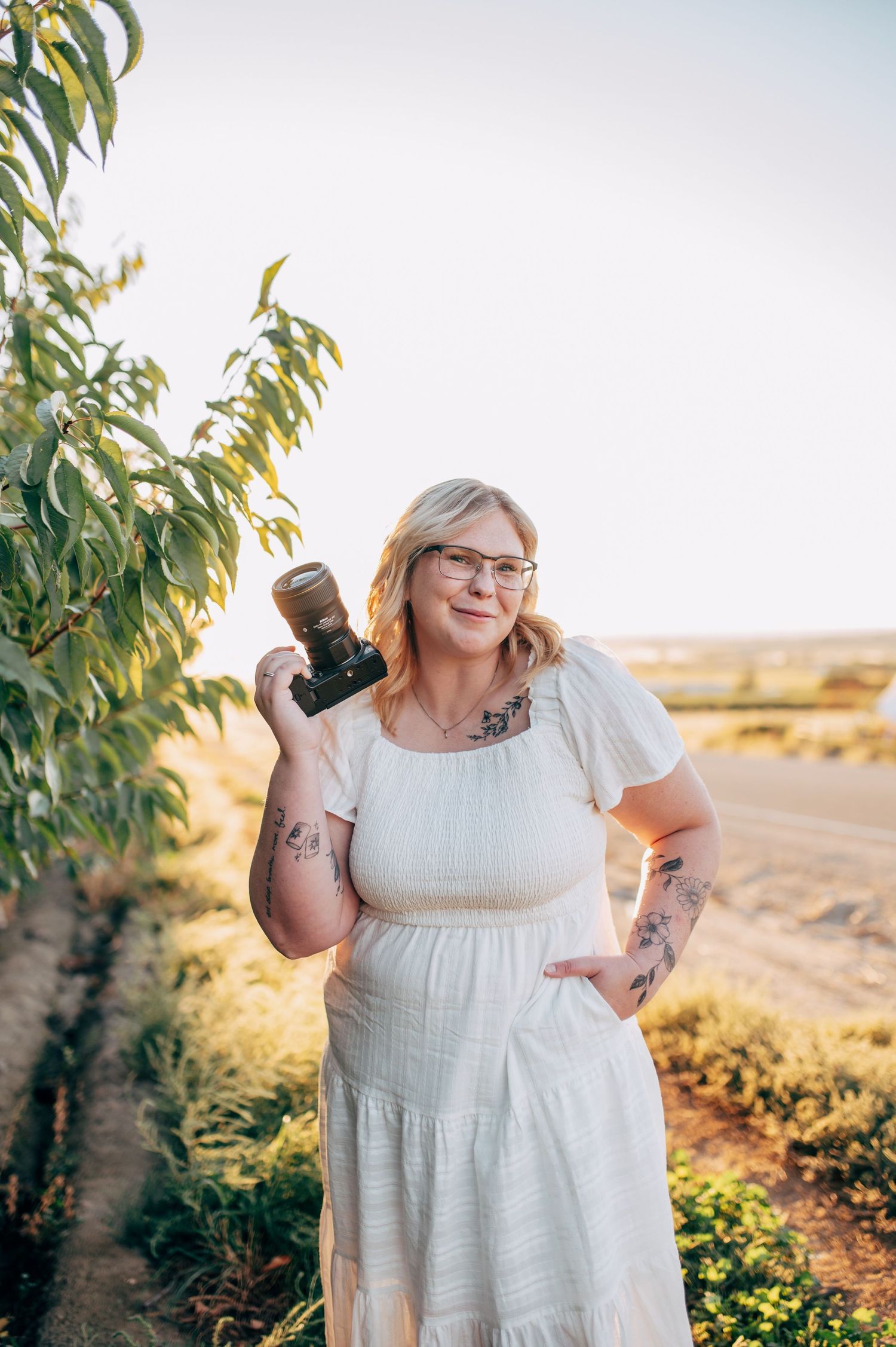 A person in a flowing white dress poses joyfully against a desert landscape during golden hour.