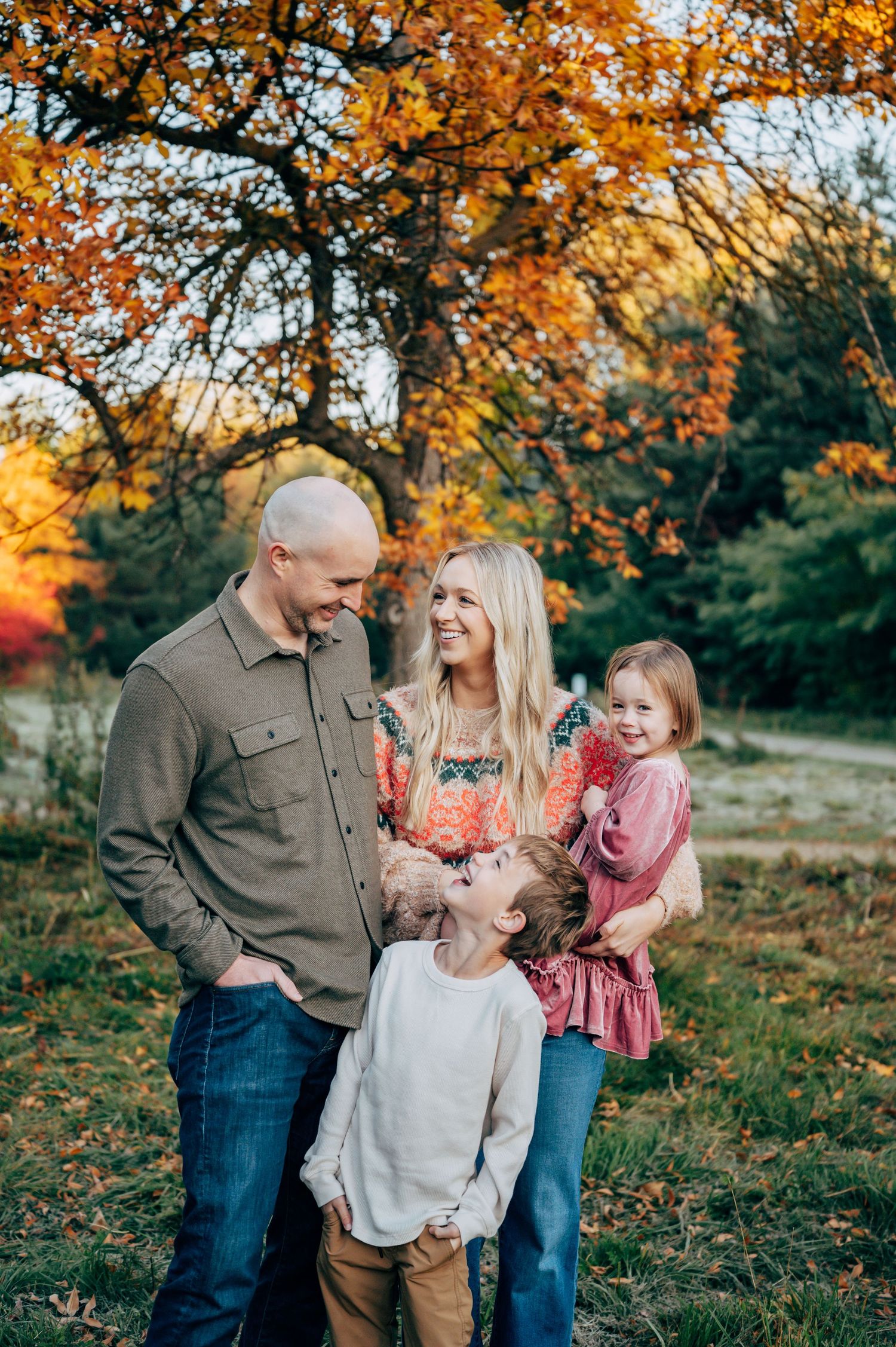 Family of four smiling together outdoors among vibrant autumn foliage during a fall portrait session.
