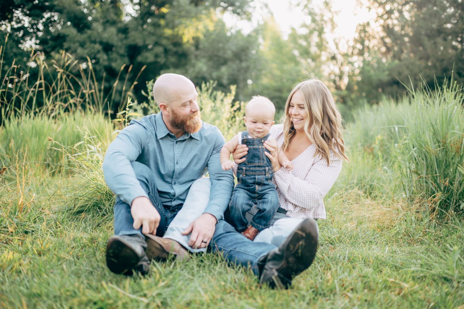 Family sitting together on grass in a sunny meadow during golden hour.