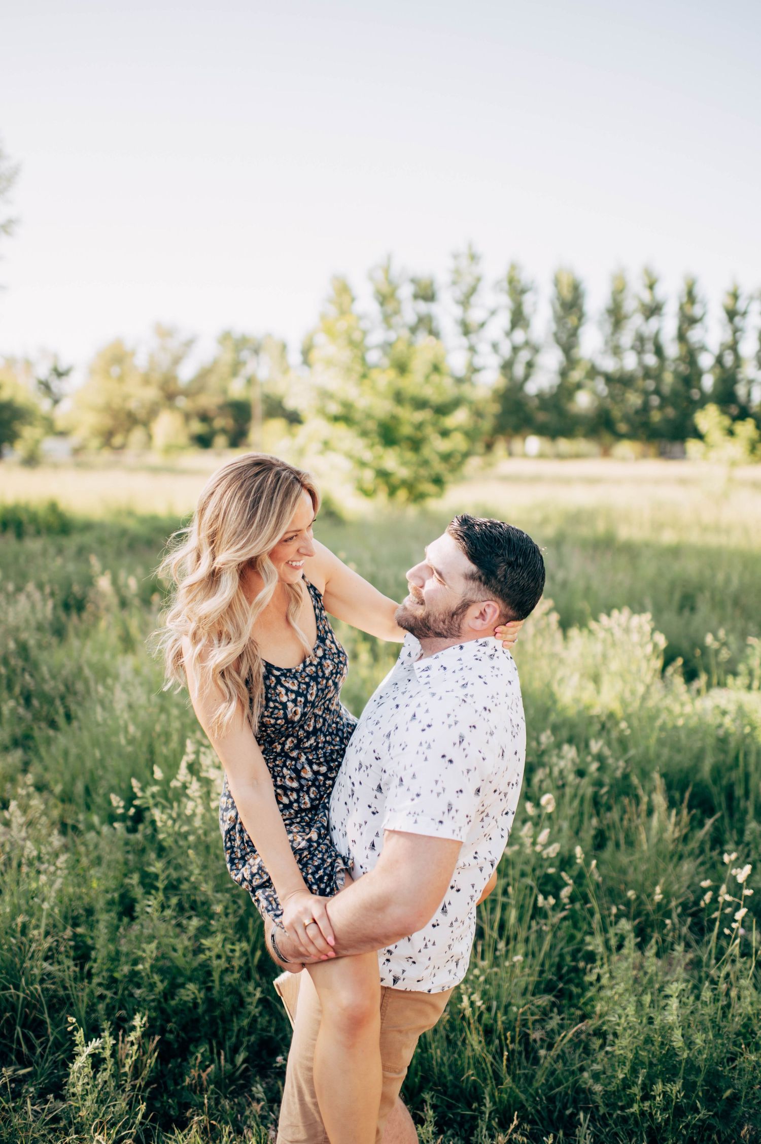 A couple holds hands and gazes at each other lovingly in a lush green field on a sunny day.