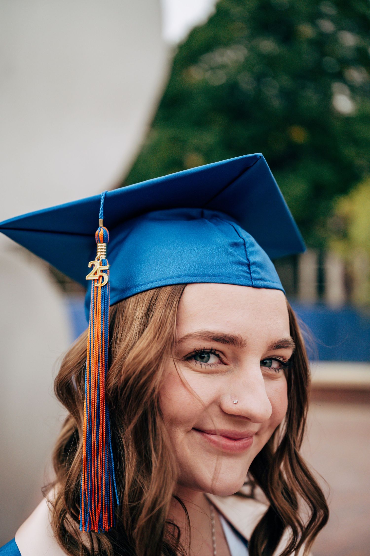 Young woman smiling in blue graduation cap with colorful tassel and '25' charm, celebrating her 2025 graduation.