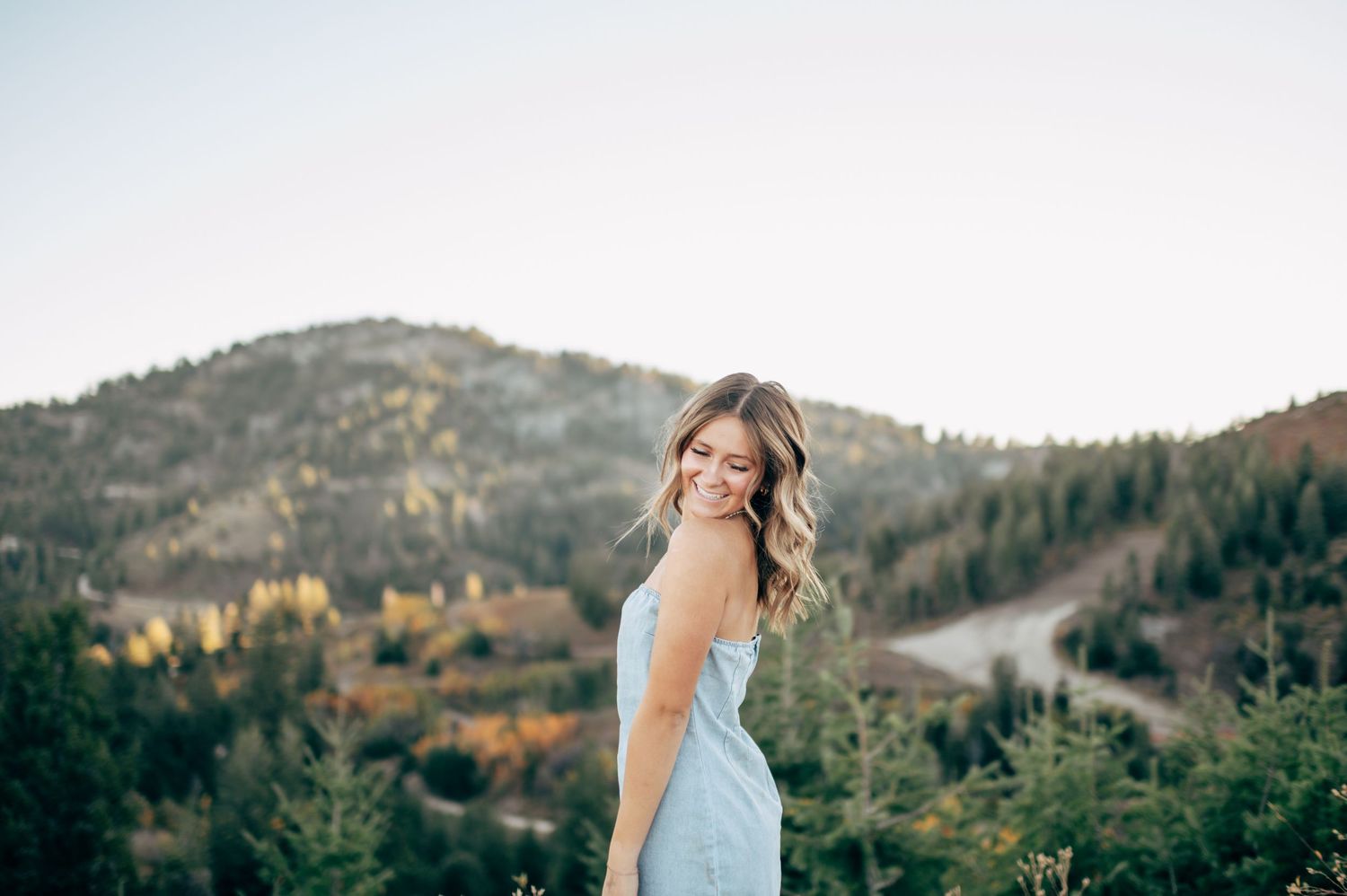 A woman in a blue dress poses against a scenic mountain backdrop at sunset.
