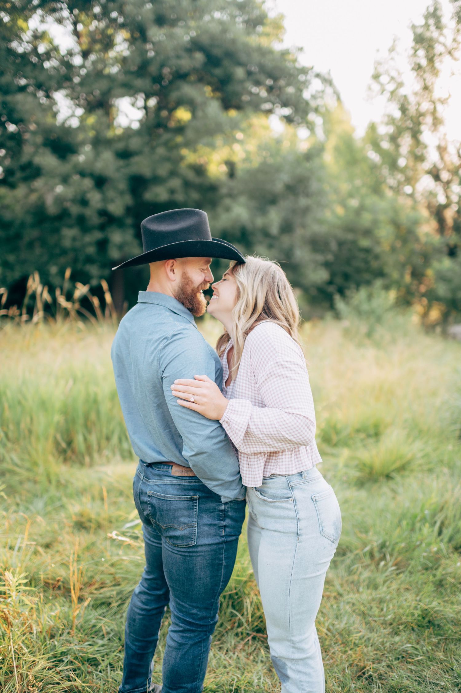 A romantic couple shares an intimate moment in a sunlit meadow with trees in the background.