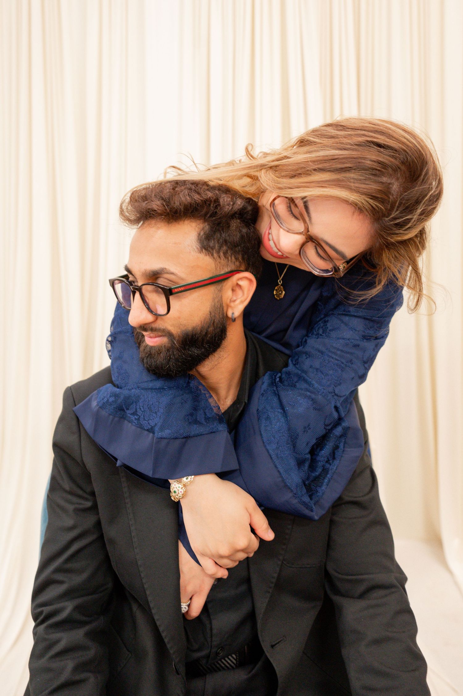 A playful embrace captured in an intimate indoor portrait session with soft curtains in the background.
