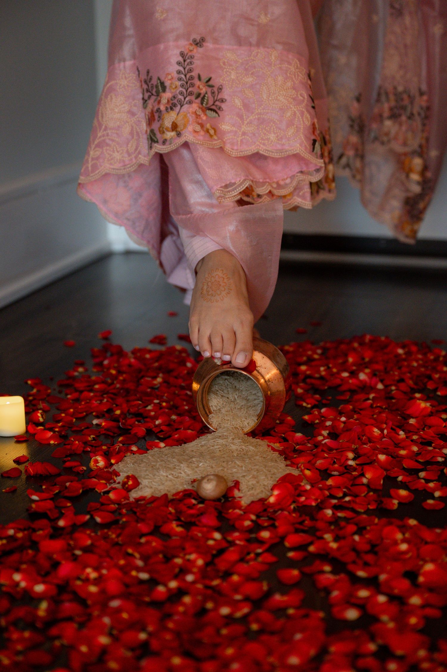 Rose petals scattered on dark floor with person in pink traditional dress visible at the edge.