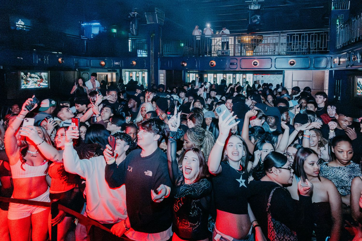 Large crowd dancing and partying in a dark nightclub with blue lighting.