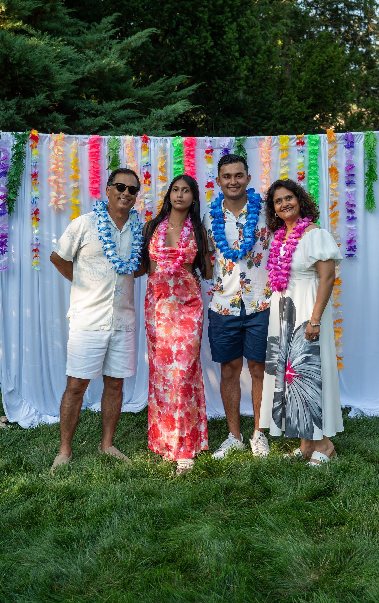 Summer party scene with guests in bright attire posed against a white backdrop with colorful hanging decorations.