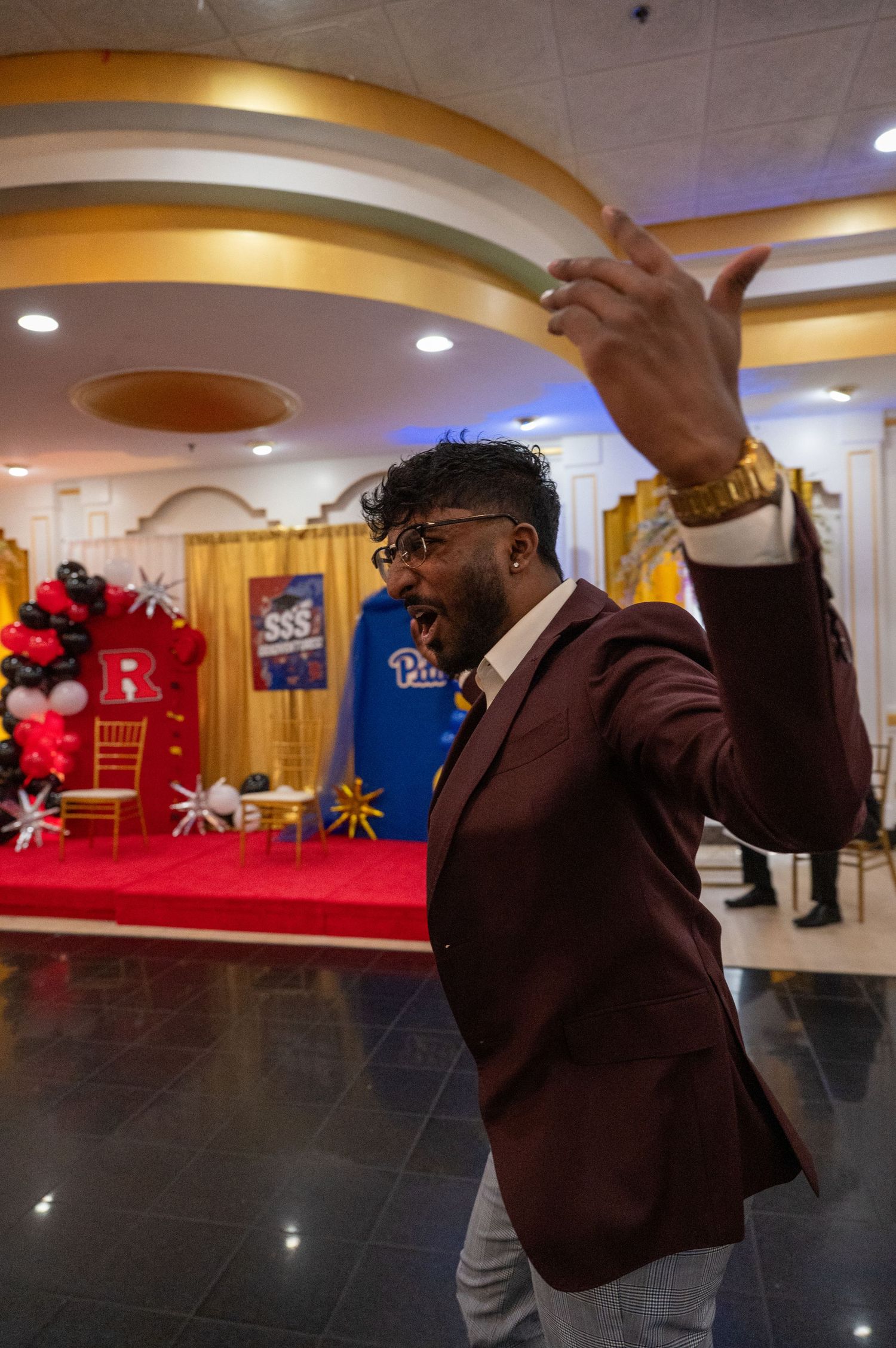 Person in burgundy blazer dancing energetically under decorative ceiling lights at an event.