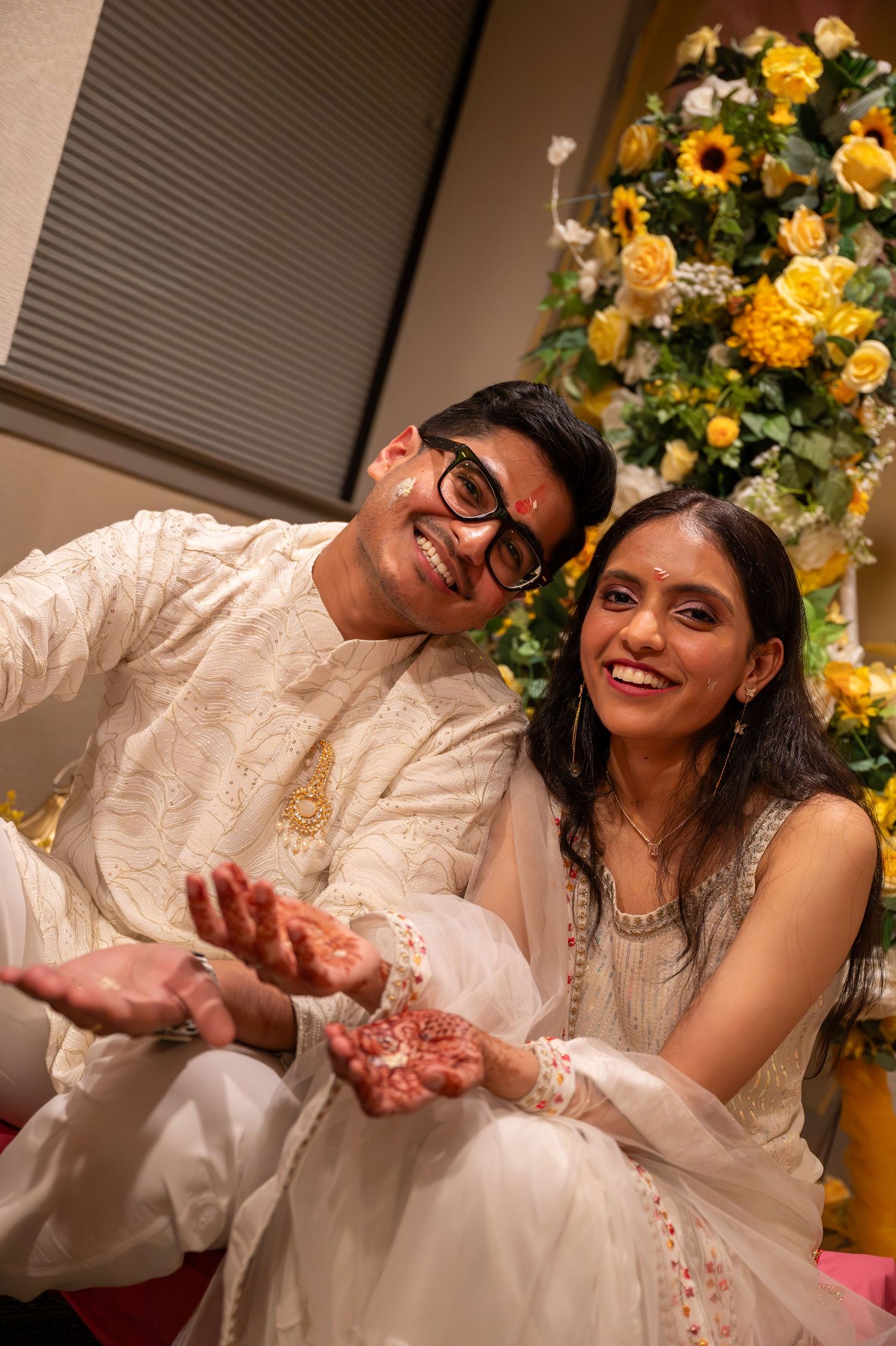 A couple shares joyful moments at their wedding celebration with yellow floral decorations in the background.