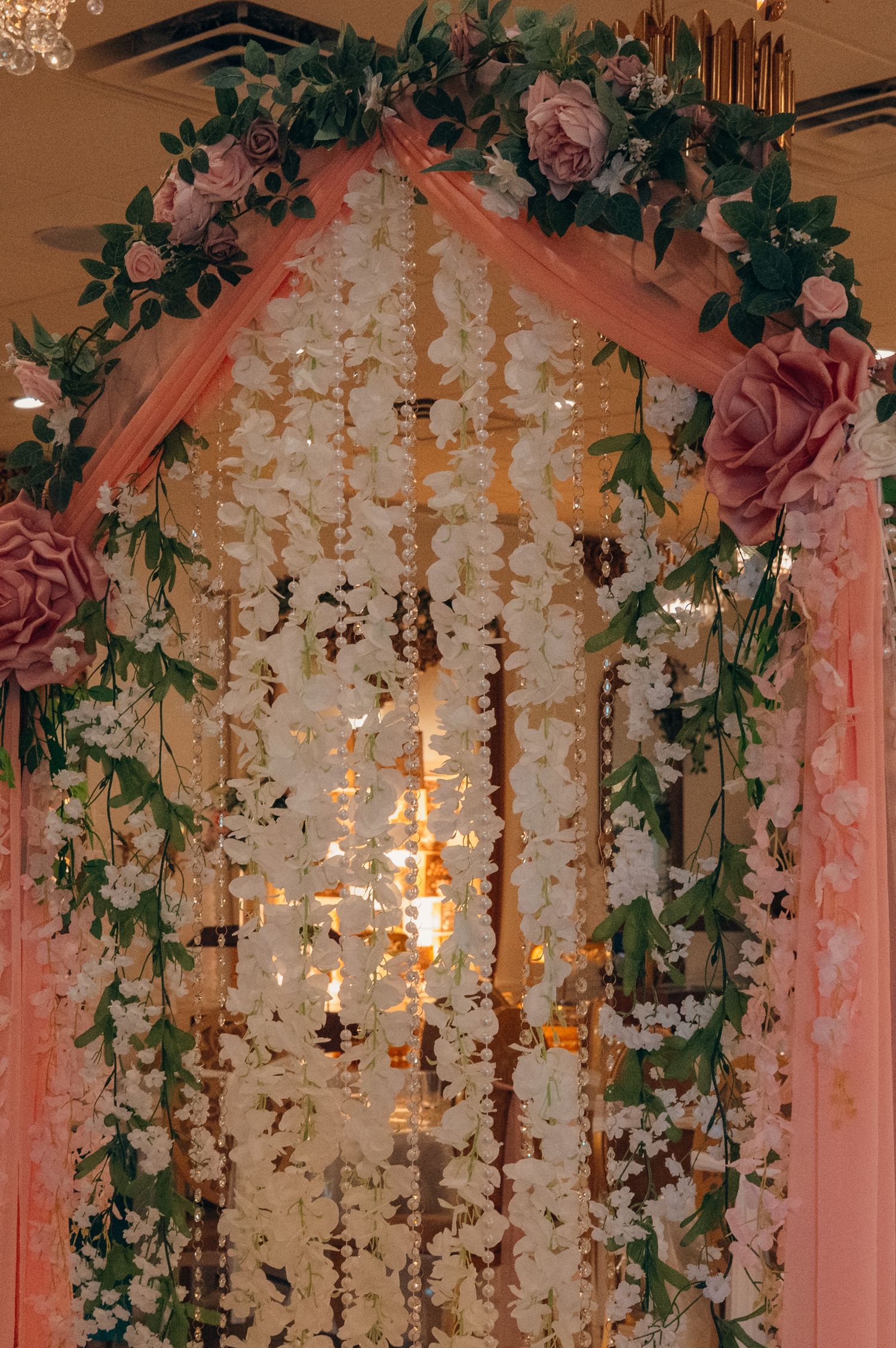 Romantic wedding venue ceiling decorated with hanging white flowers and pink drapery.