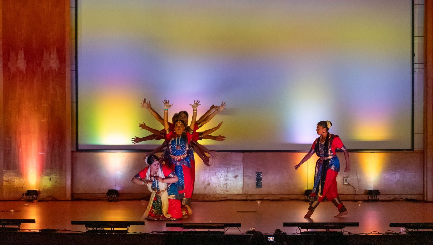 Performers execute synchronized dance moves on stage with vibrant lighting effects.