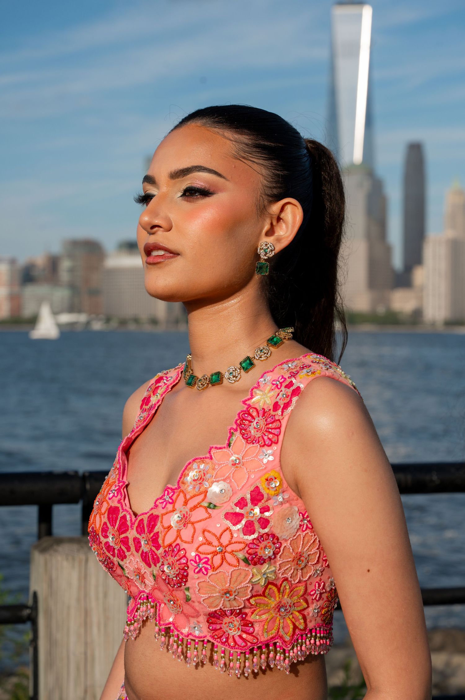 Close-up portrait of woman in pink embellished dress with NYC skyline in background.