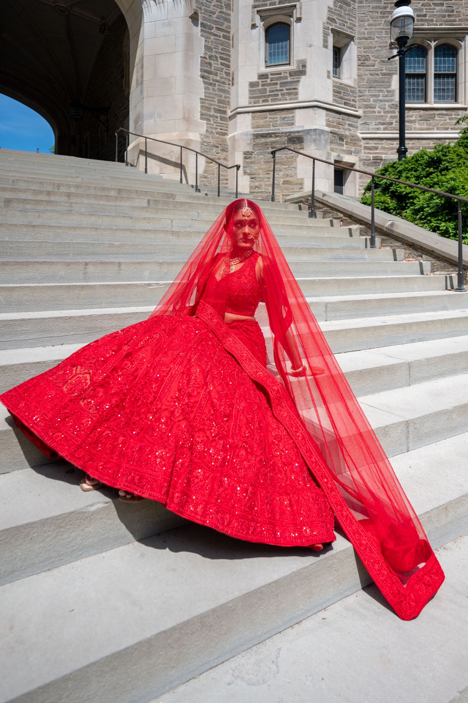 A dramatic red ballgown with tulle overlay creates sweeping shapes against stone steps.
