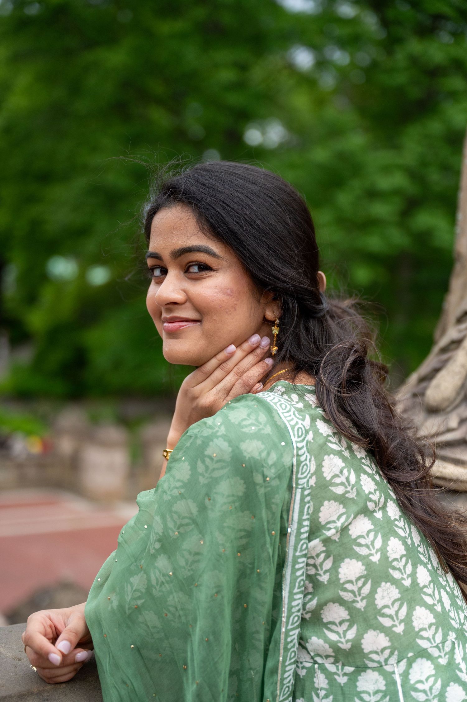 Woman in mint green traditional dress poses outdoors against natural background.