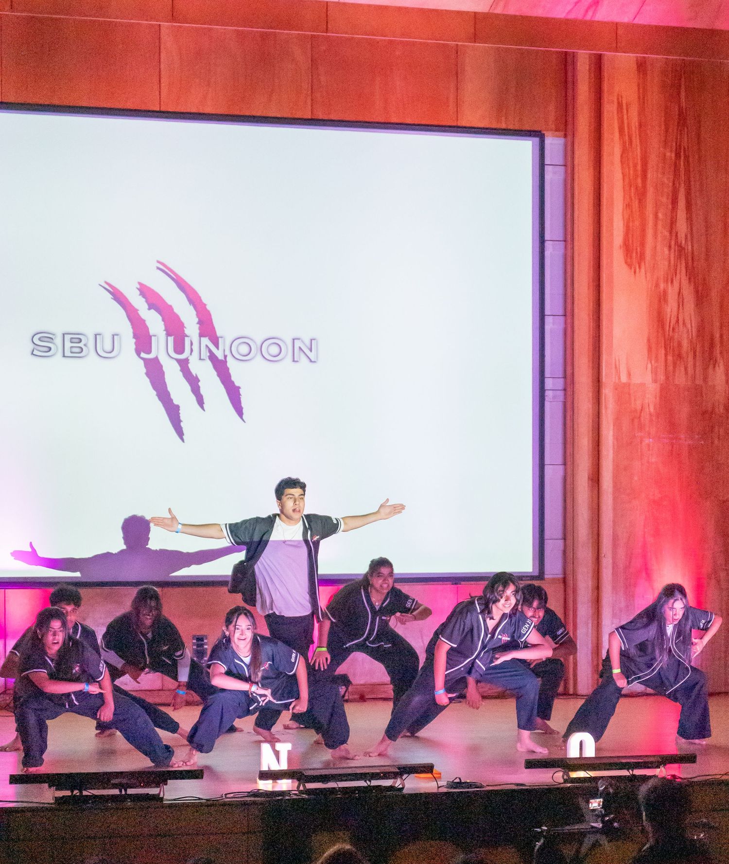 Performers create a dramatic sequence of movements on stage with red ambient lighting.