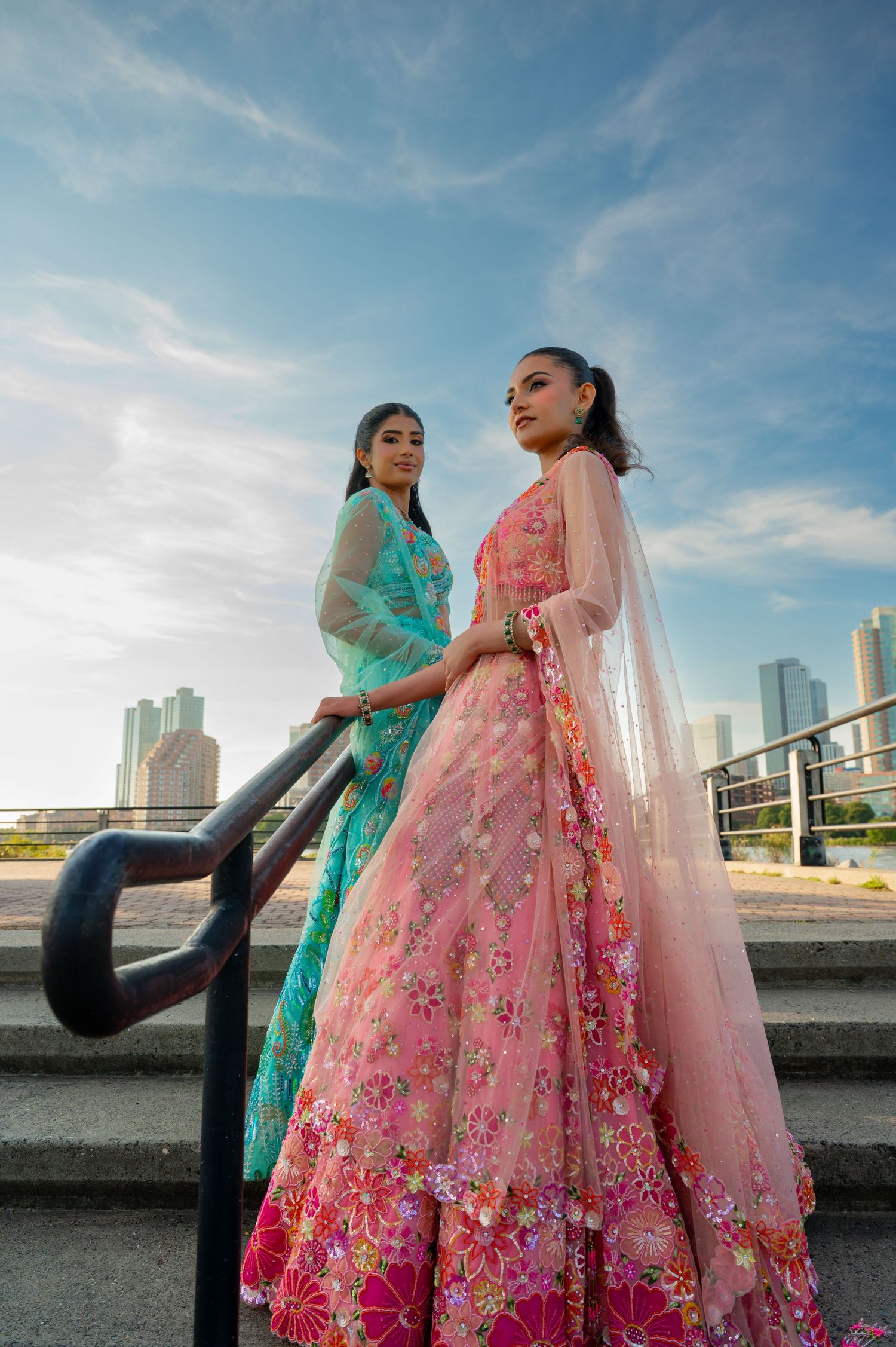 Models in vibrant lehengas with flowing dupattas pose against urban backdrop.