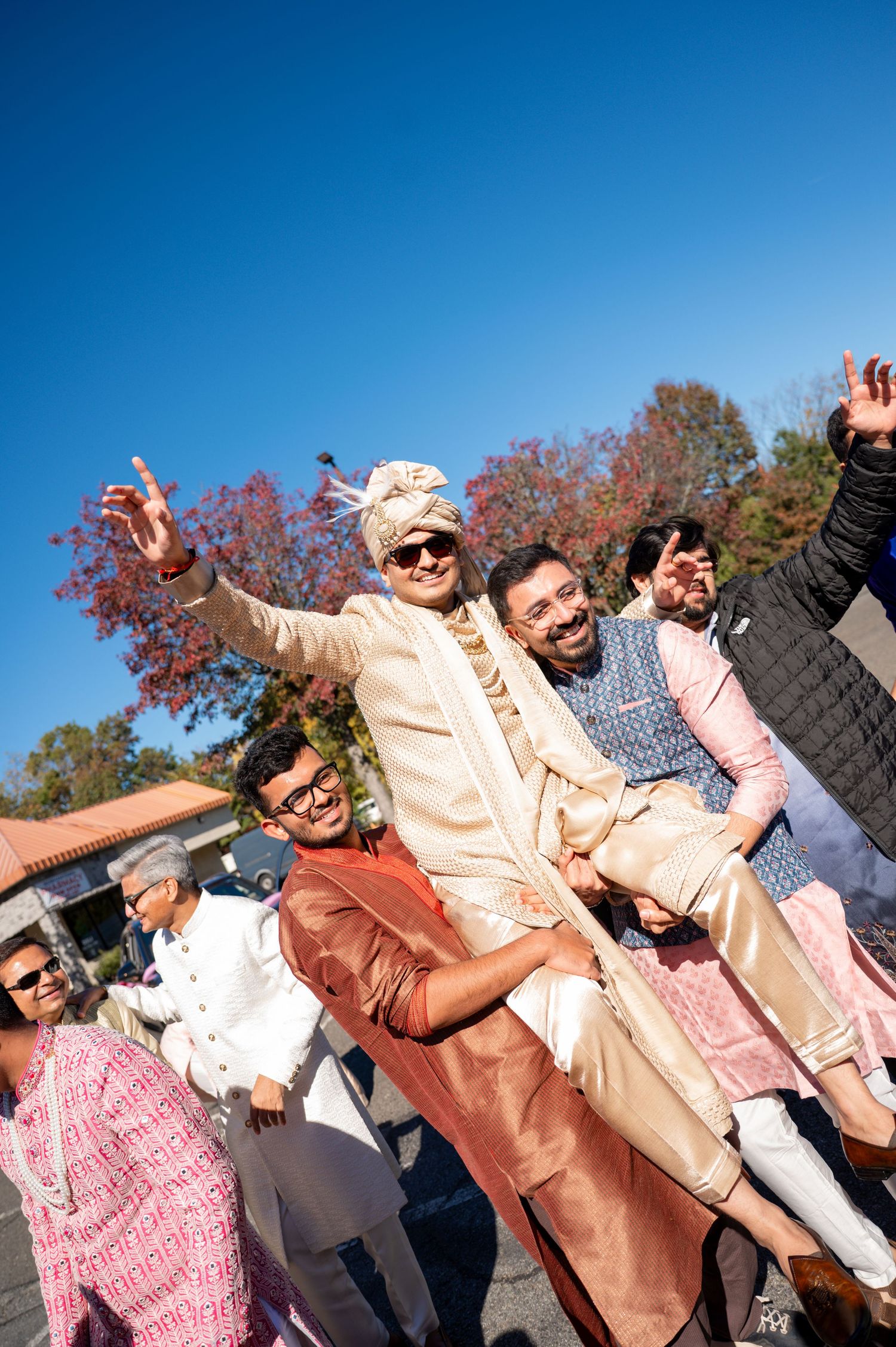 Wedding guests in peach and pink outfits celebrating joyfully under blue sky.