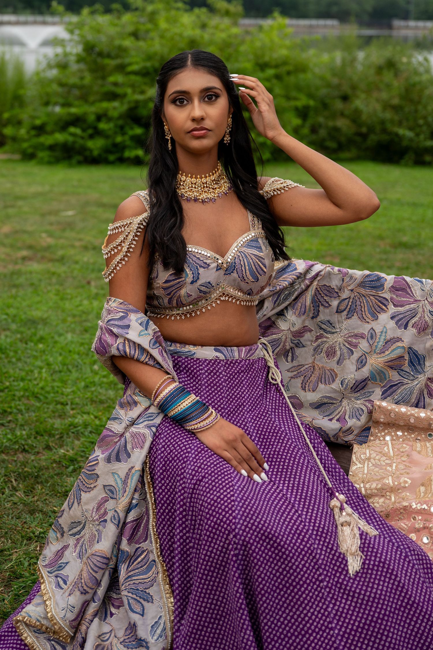 Model in purple and floral formal wear poses elegantly on grass.