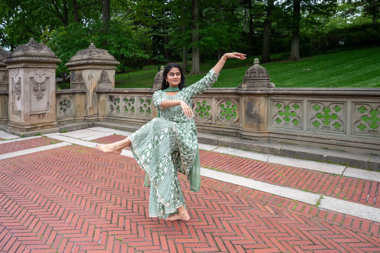 Figure in flowing mint green dress dances gracefully outdoors near stone architecture.