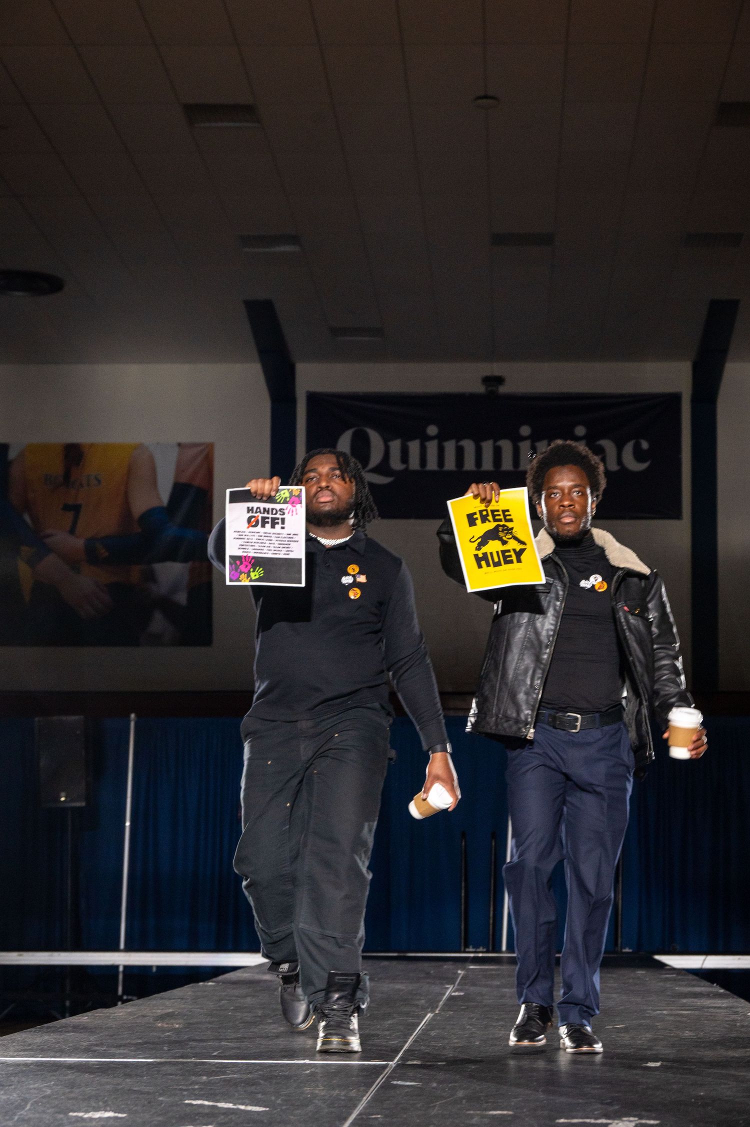Performers hold protest signs while moving across a dimly lit stage.