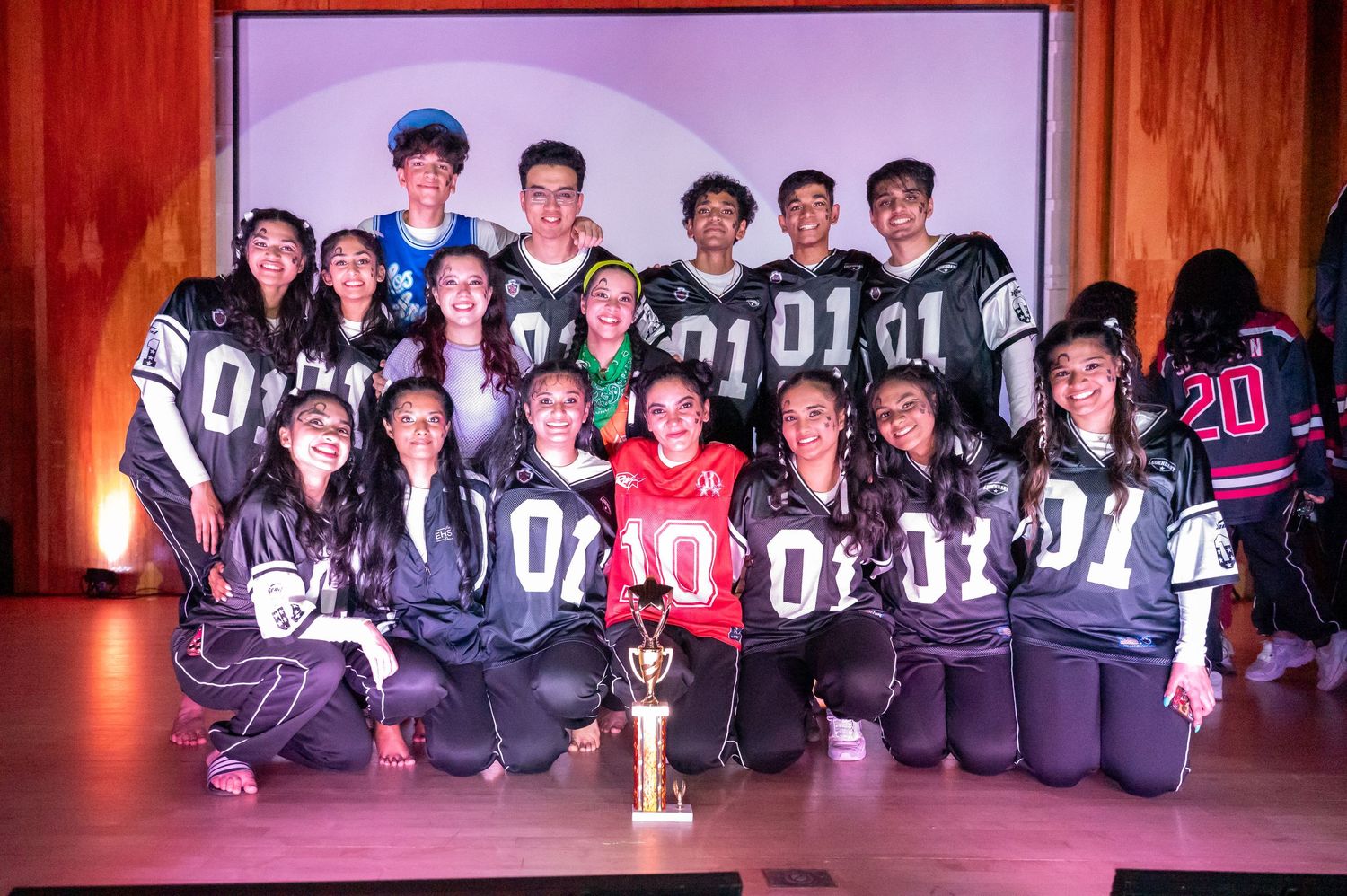 Dance team poses together wearing matching jerseys for a group photo.