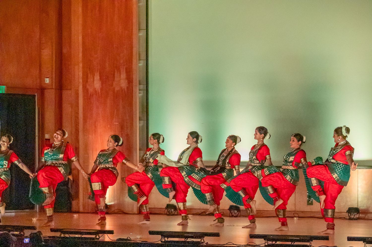 Dancers in red costumes perform a synchronized routine on stage.