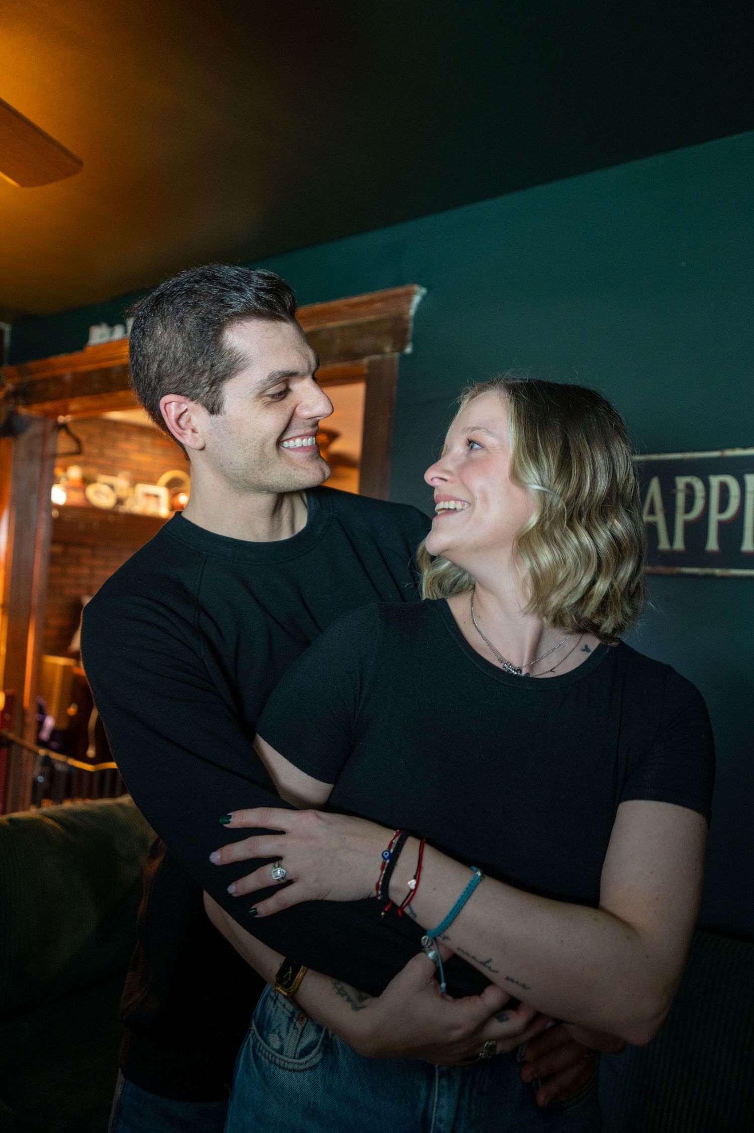 A couple in black clothing share a tender moment together in a dimly lit room.