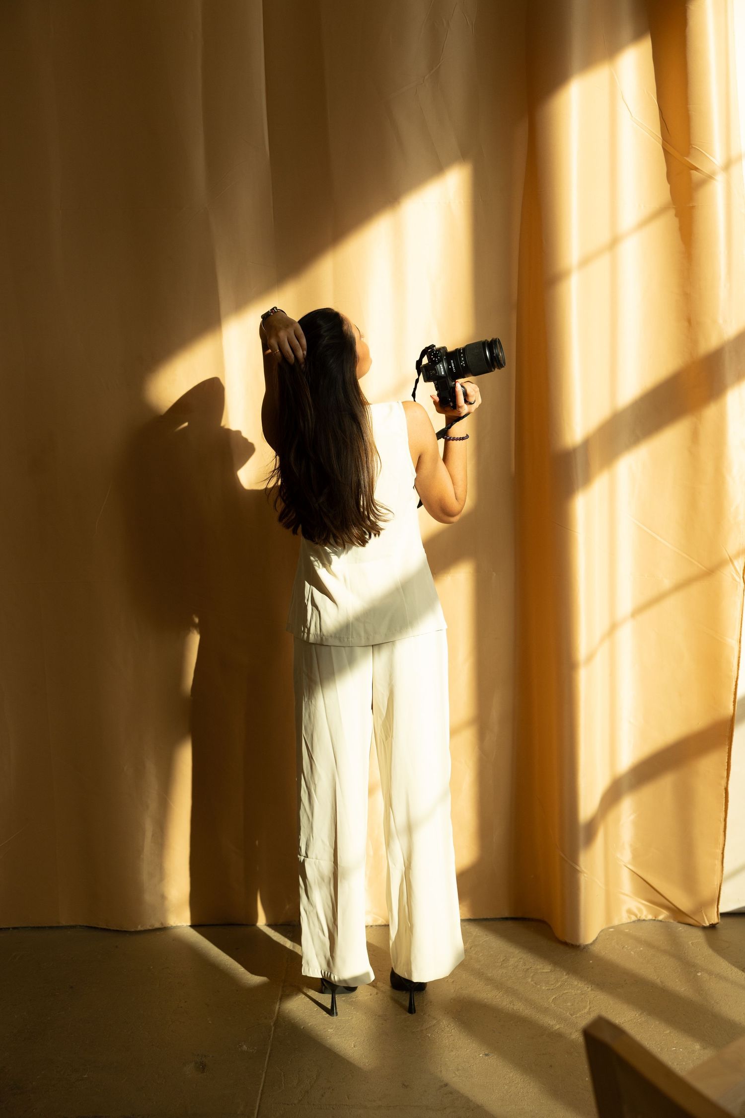 Artistic silhouettes of a photographer at work against warm sunlit curtains.