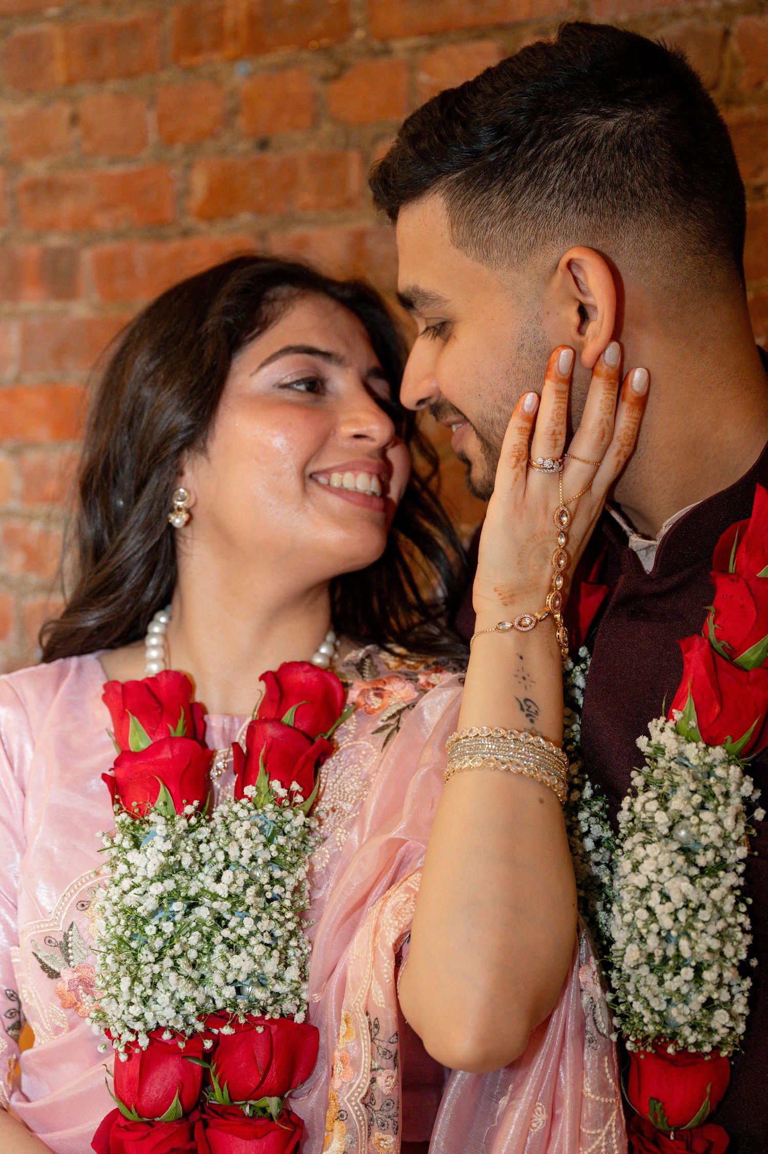 A romantic couple shares tender moments with red roses and baby's breath flowers against a brick wall backdrop.