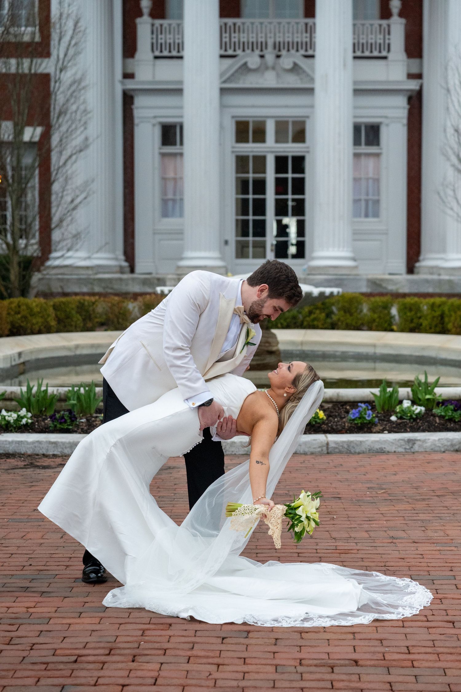A romantic dip pose captured in sequence on red brick pavement with white columns of a building in the background.