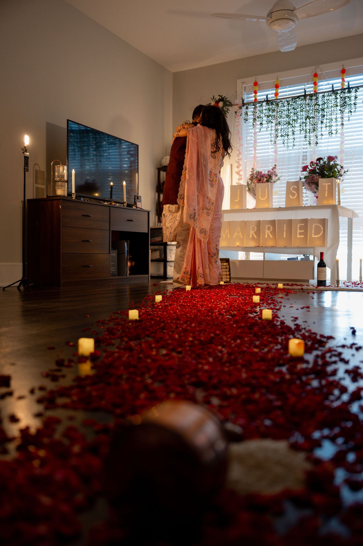 A romantic room setup with scattered red rose petals on the floor and glowing candles creating an intimate atmosphere.