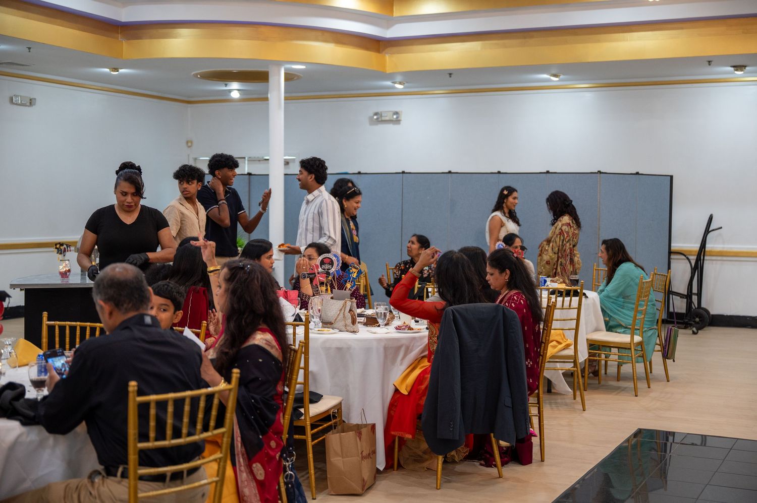Guests seated at round tables with white tablecloths in a banquet hall with orange and gold ceiling accents.