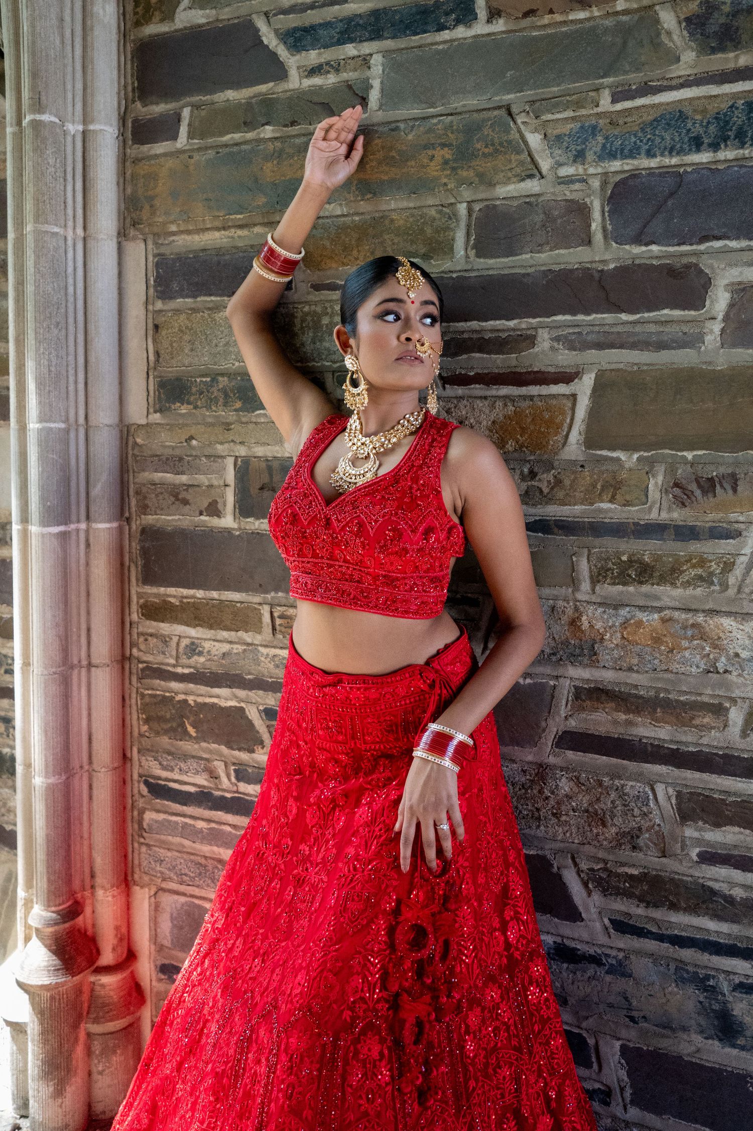 Dramatic poses in a red sequined gown against stone wall architecture.