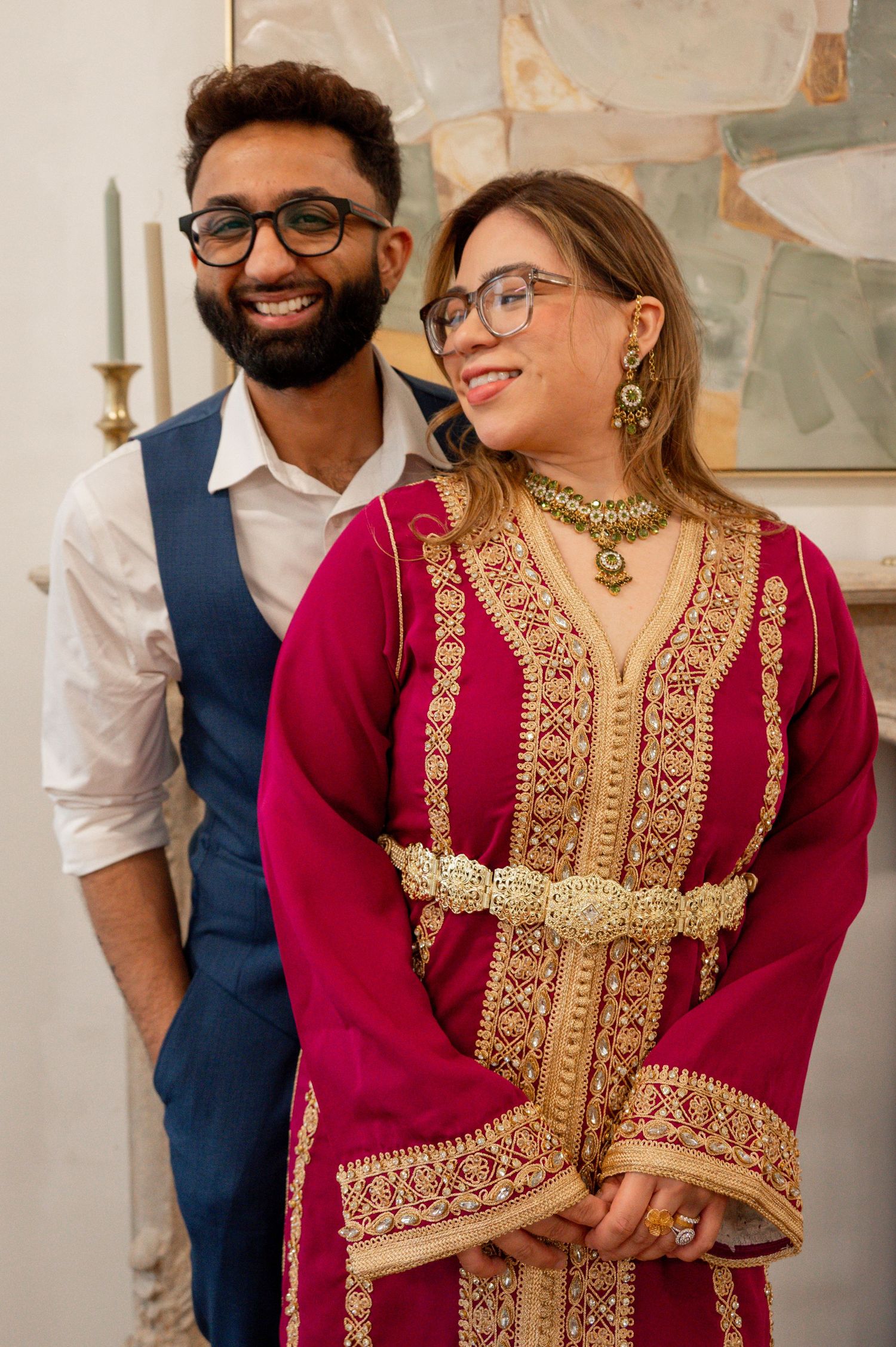 A couple wearing formal attire poses together against an abstract art background.