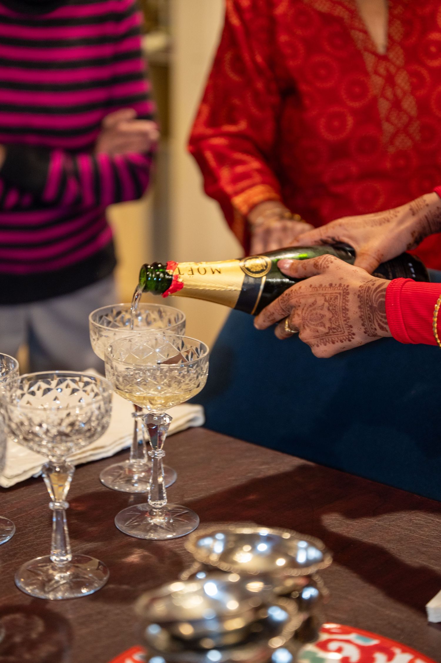 Champagne being poured into vintage crystal coupe glasses on a wooden table during a celebration.