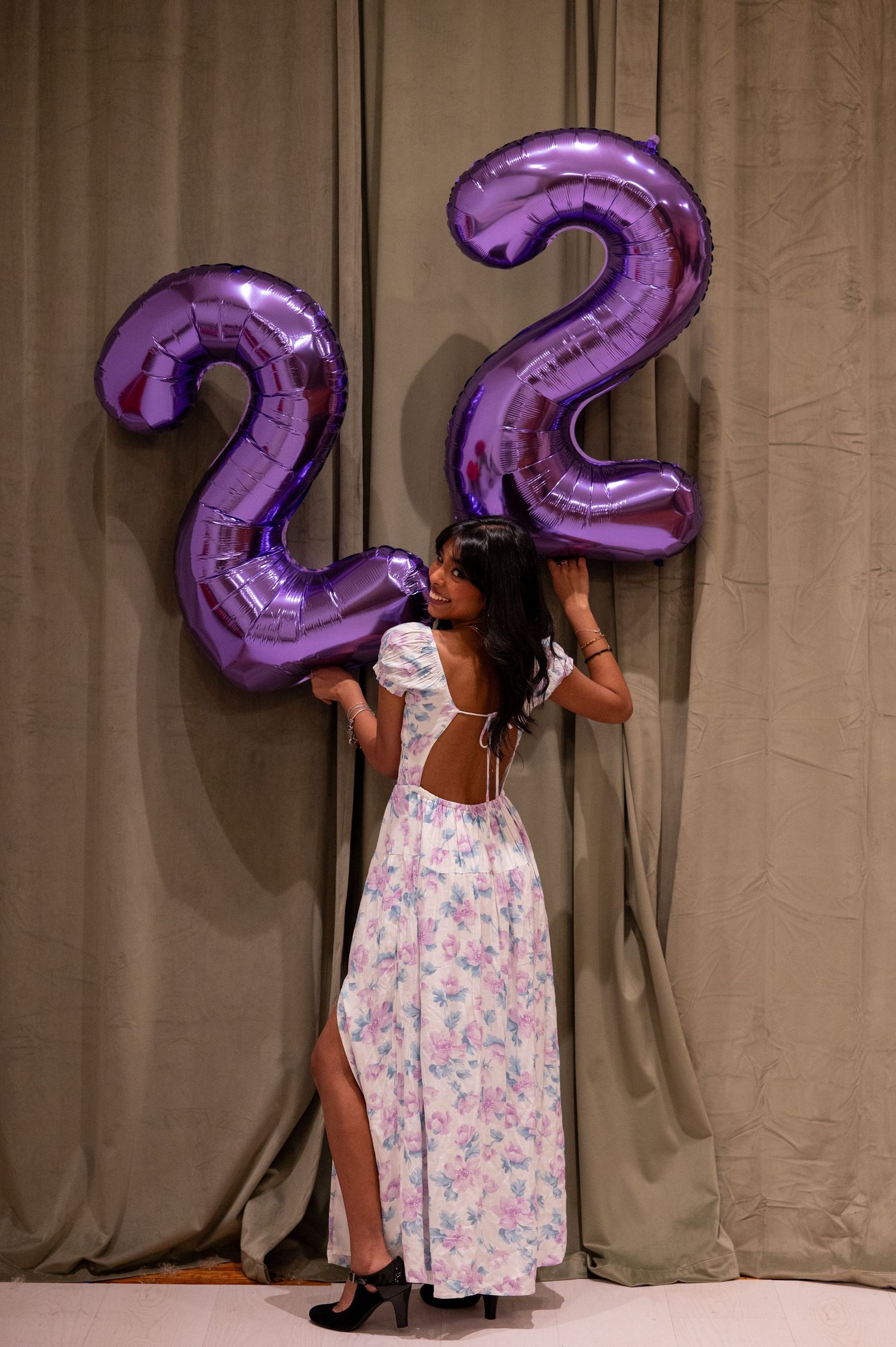 A person holding large purple number balloons against a grey curtain backdrop.