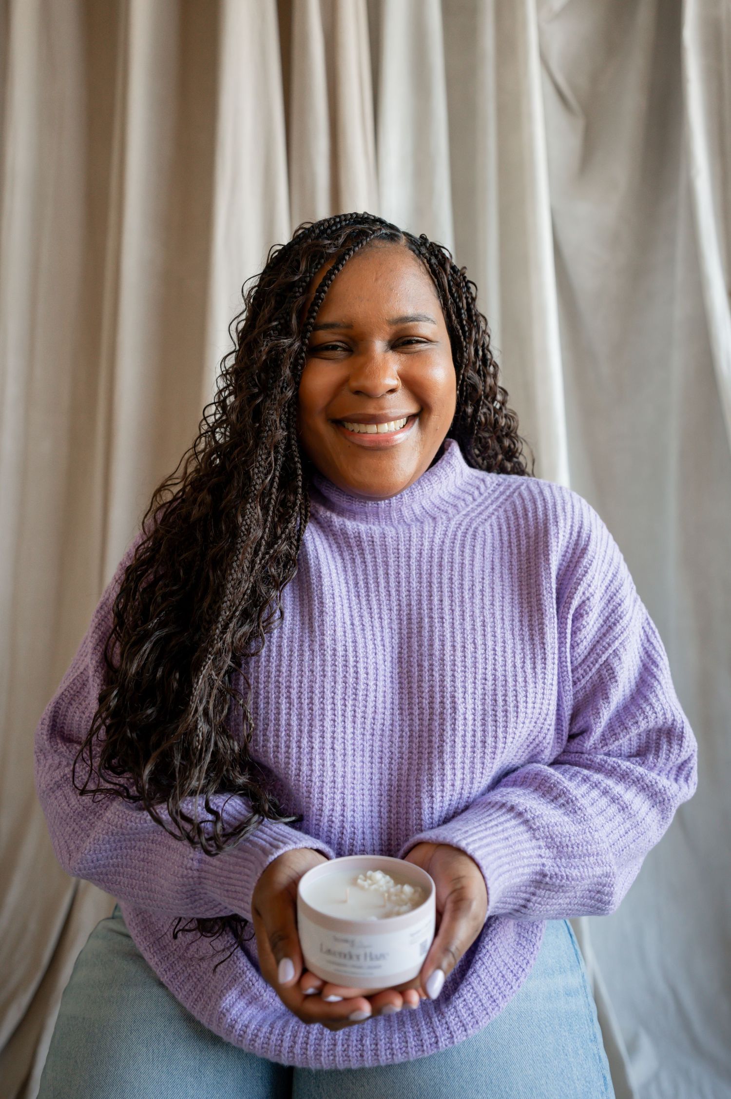 Person in lavender sweater holding white candle against light backdrop.