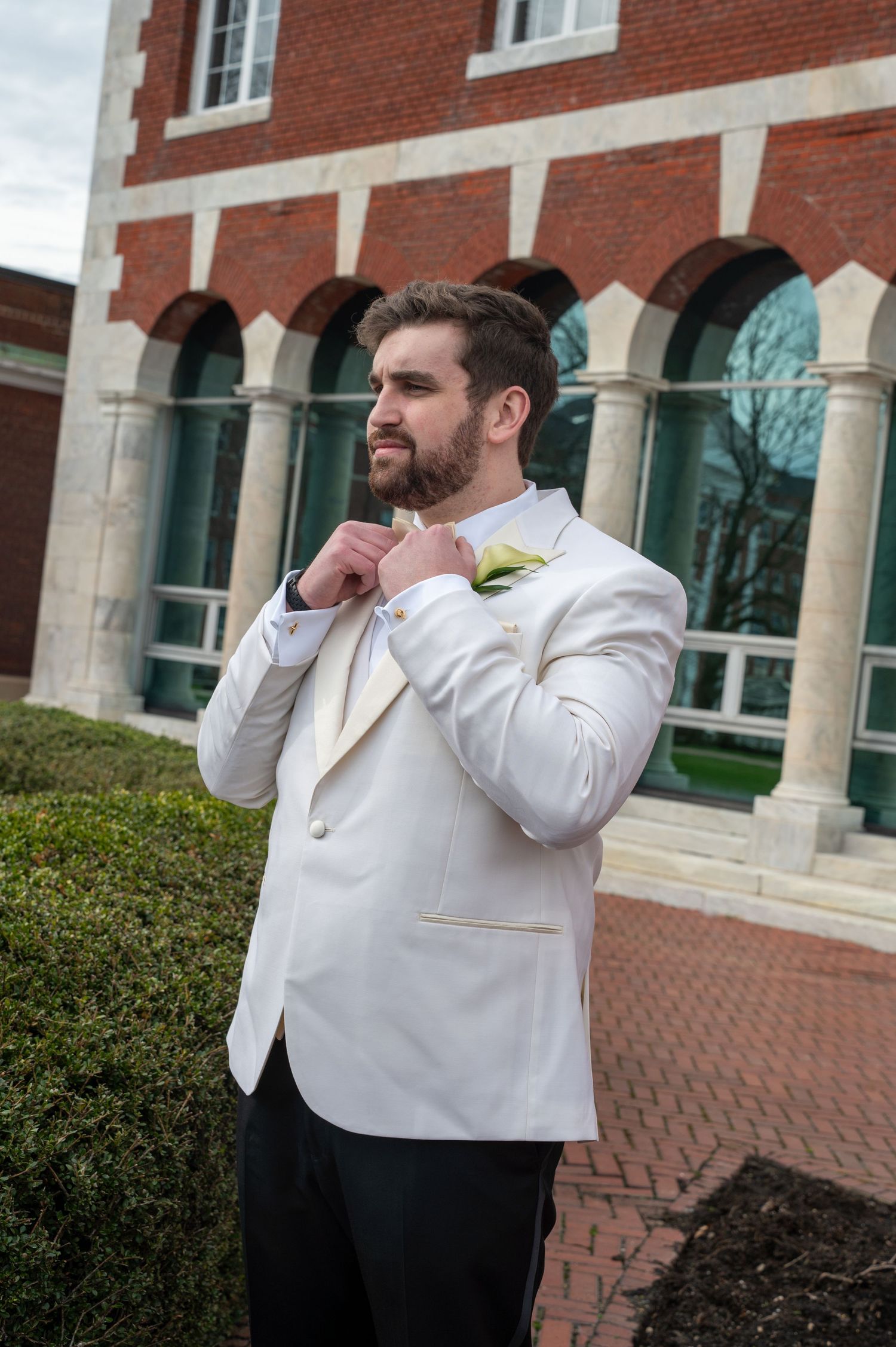 Someone in a white dress shirt laughs while standing outside a brick building with white trim and windows.