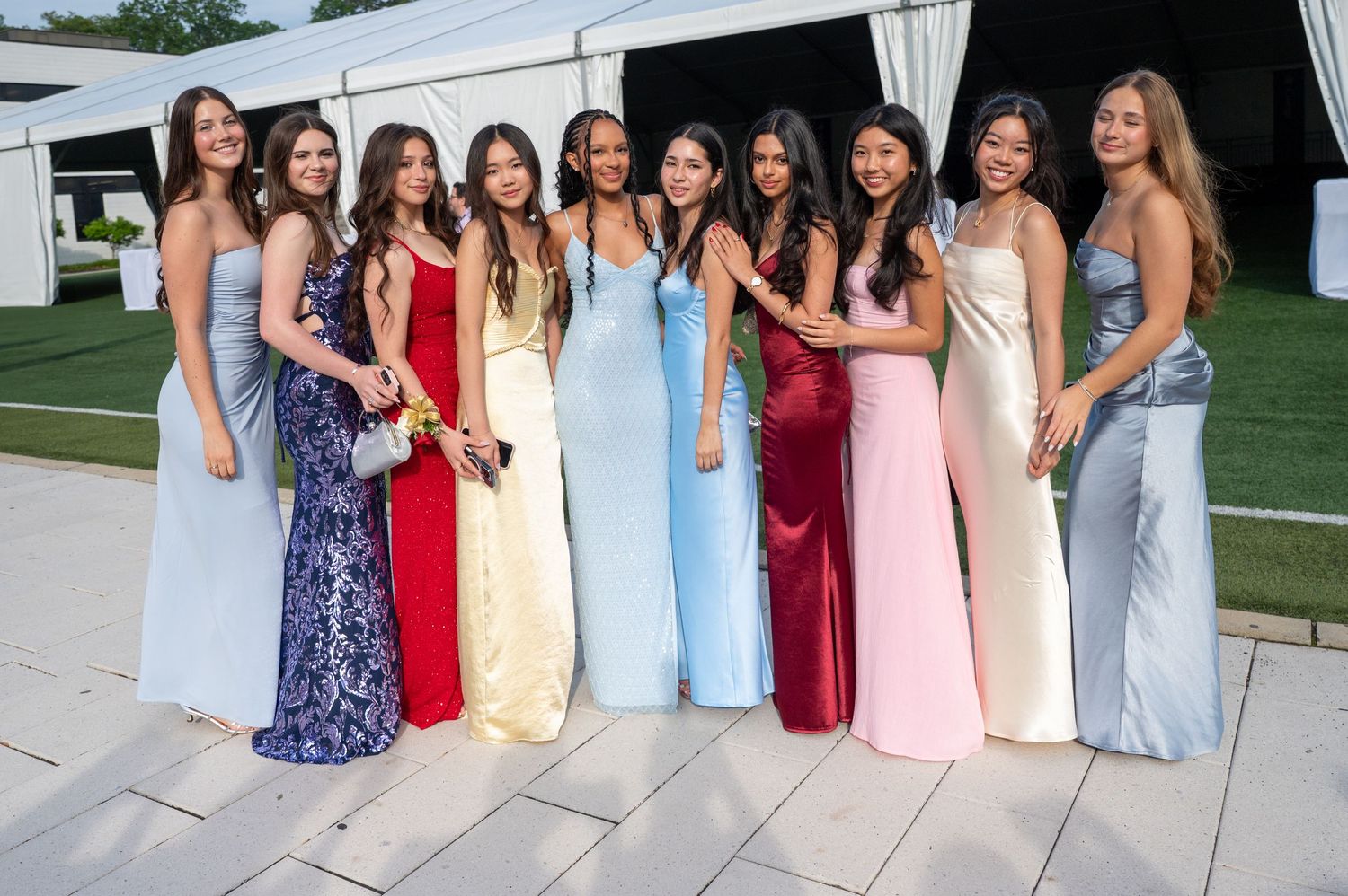 A group of people in formal evening gowns pose together at an outdoor event.