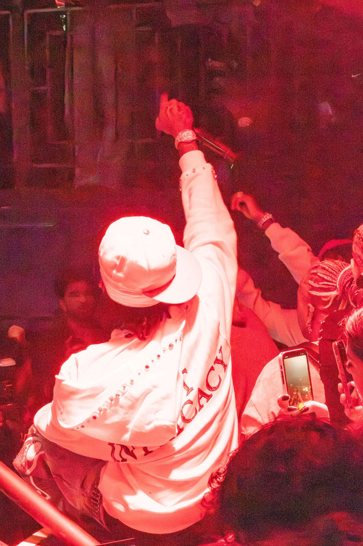 Performer in white clothing energetically entertaining a crowd under red stage lighting.