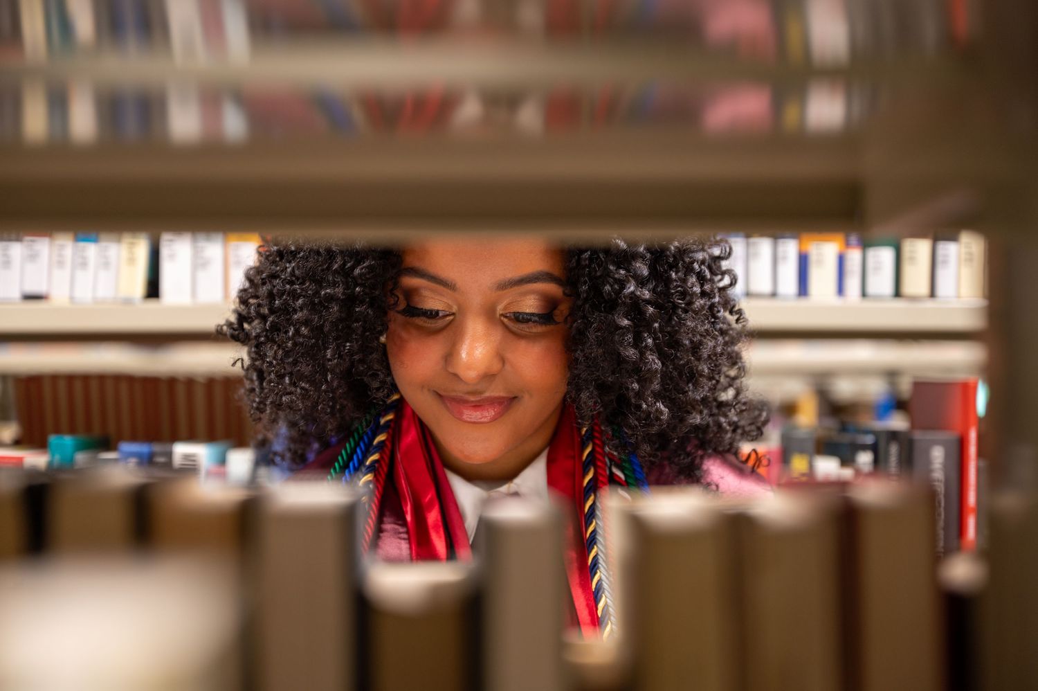 A creative library photoshoot showing someone peeking through rows of books.
