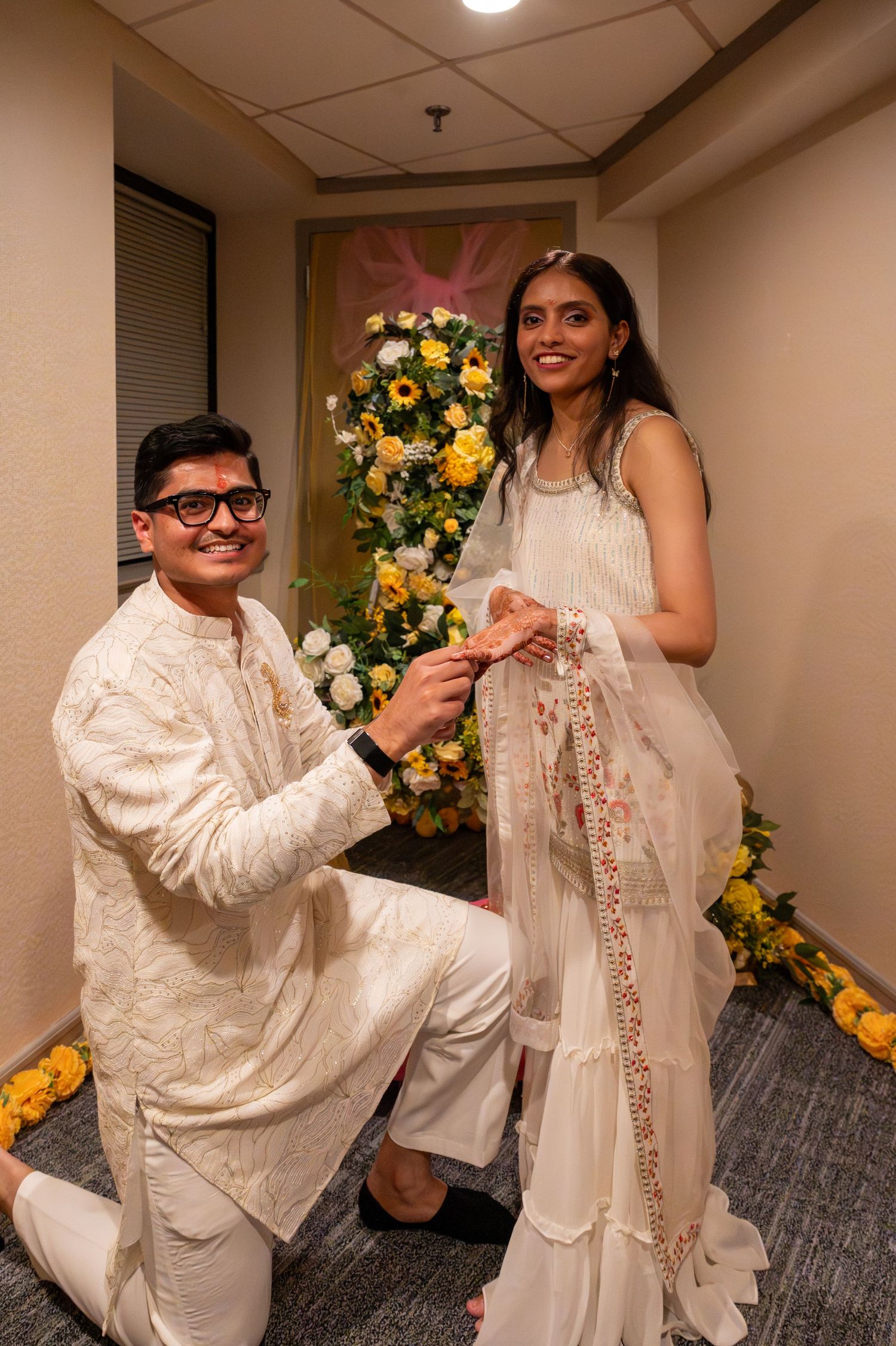A couple shares a sweet moment during a proposal in a hallway decorated with yellow and pink floral arrangements.