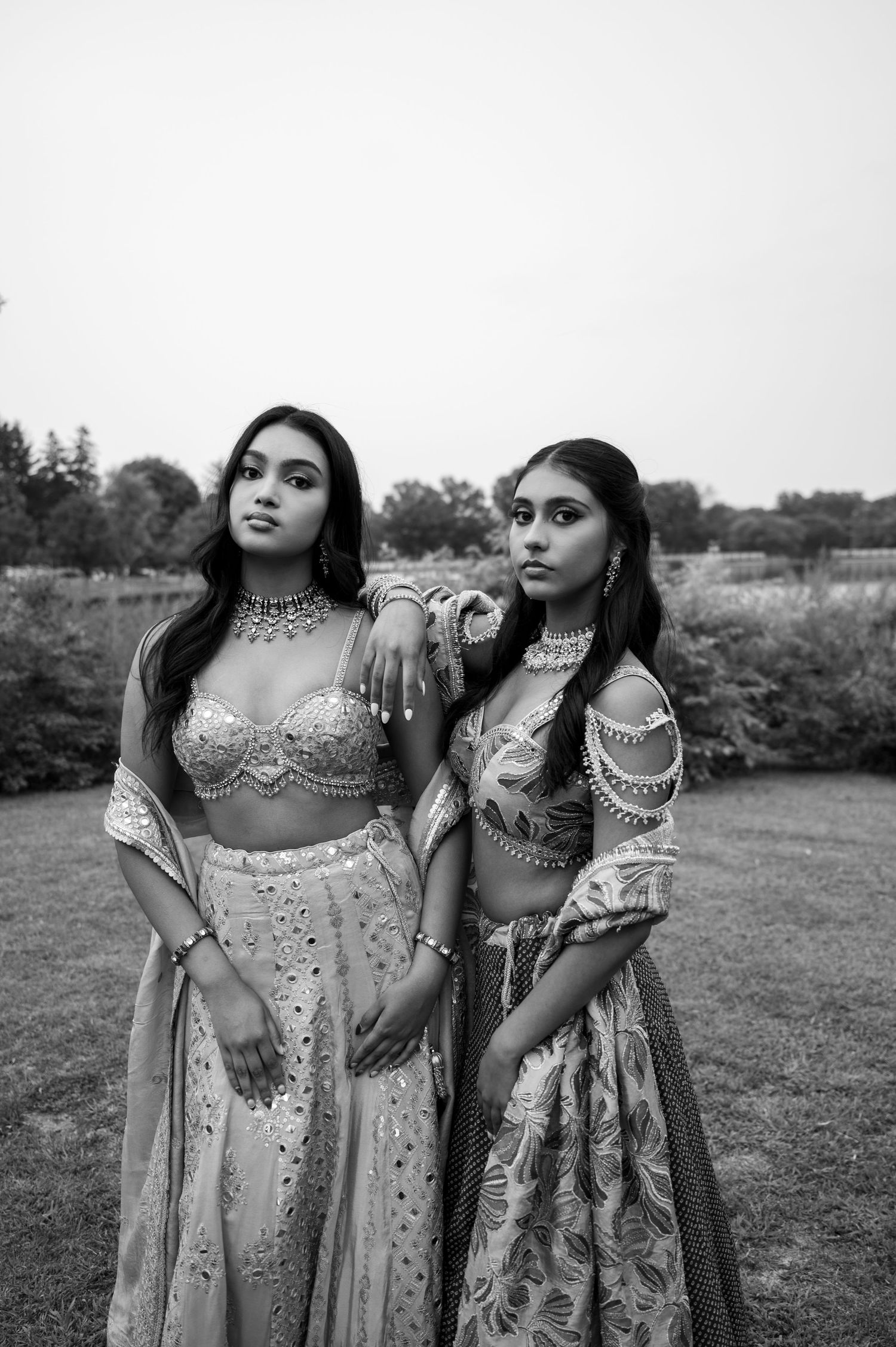 Black and white portrait of women in embellished Indian formal wear outdoors.