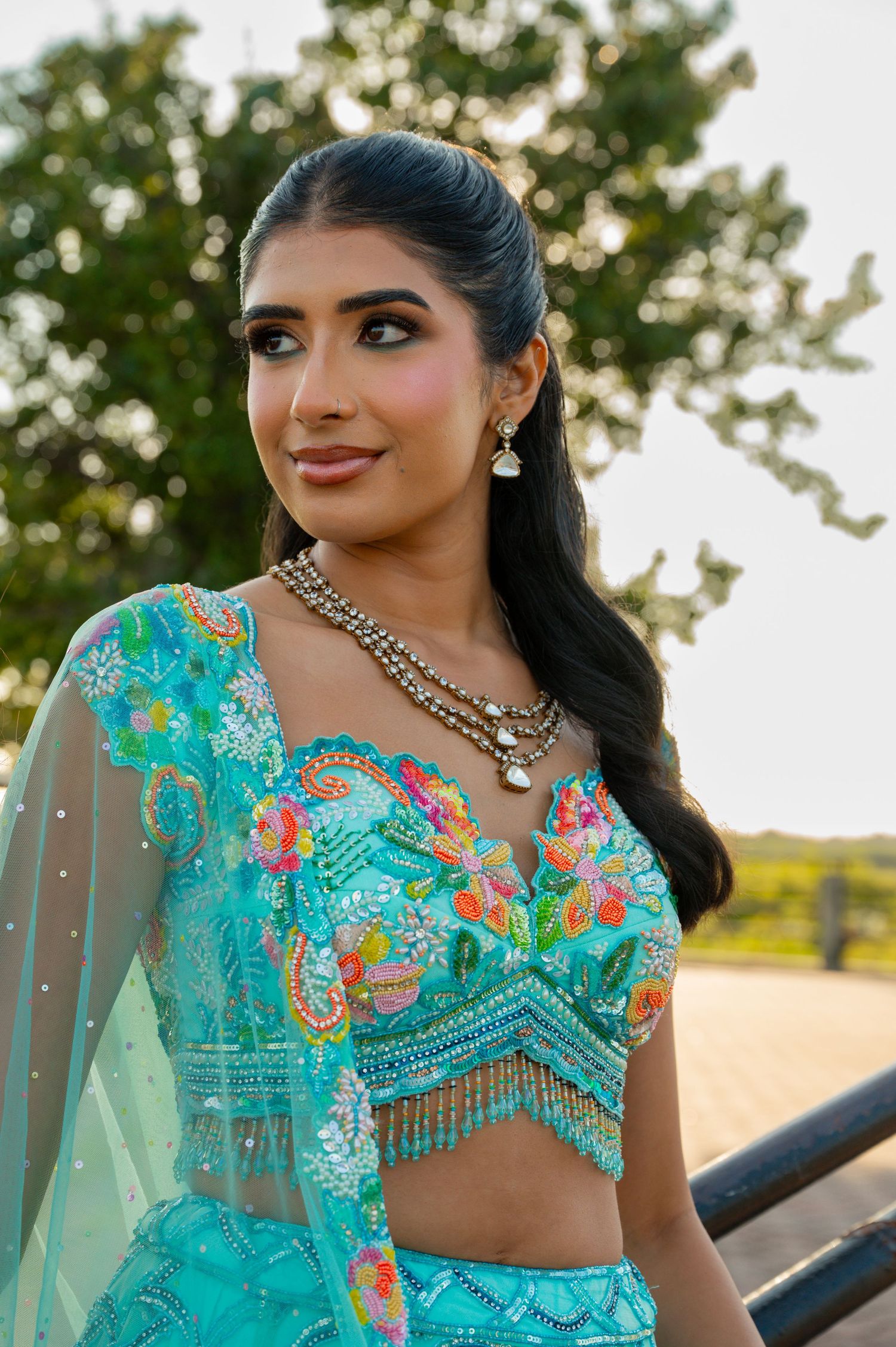Woman in turquoise embellished Indian outfit with jewelry poses outdoors.