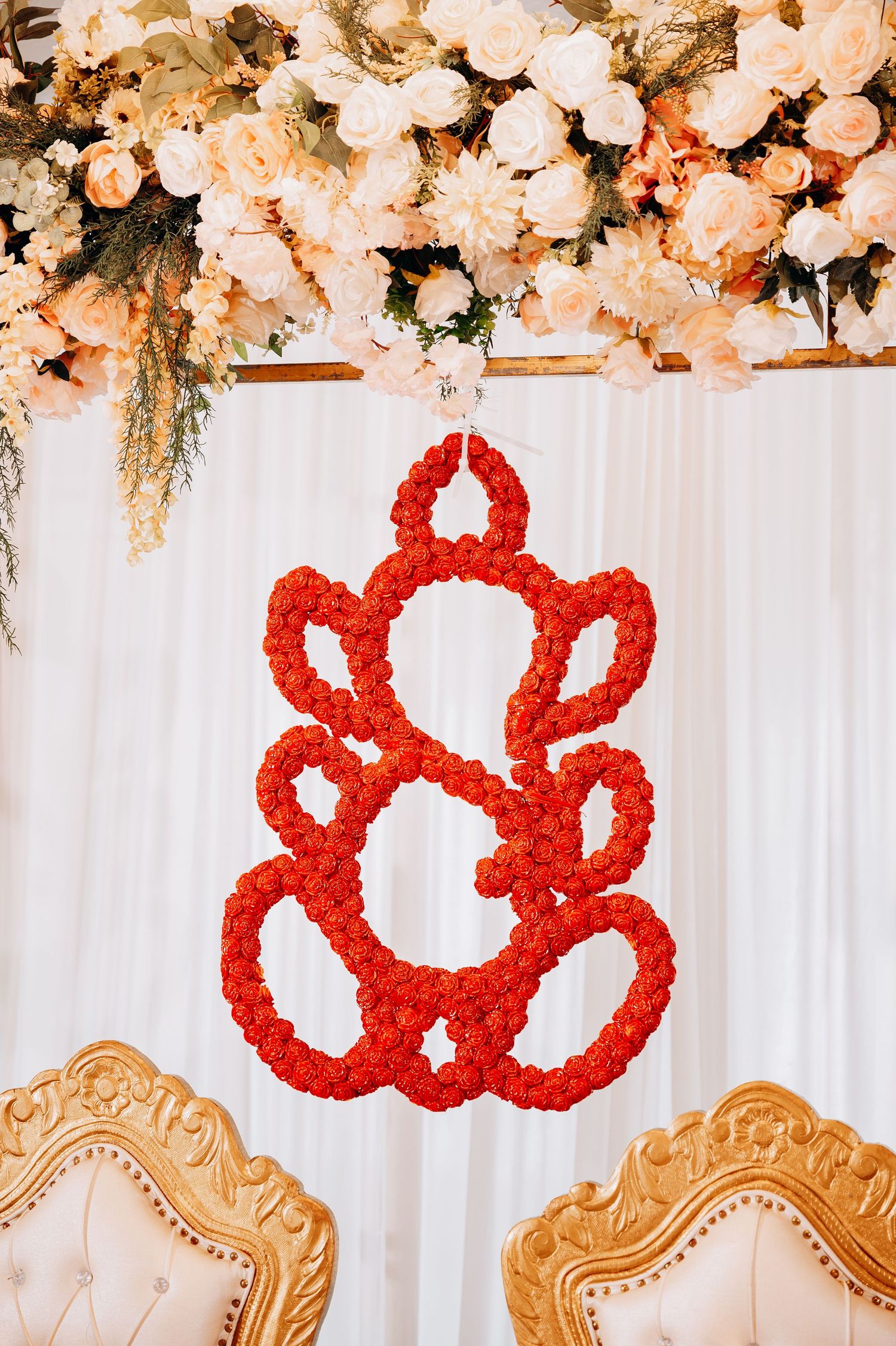Elegant wedding backdrop with white flowers and red decorative elements against a white curtain.