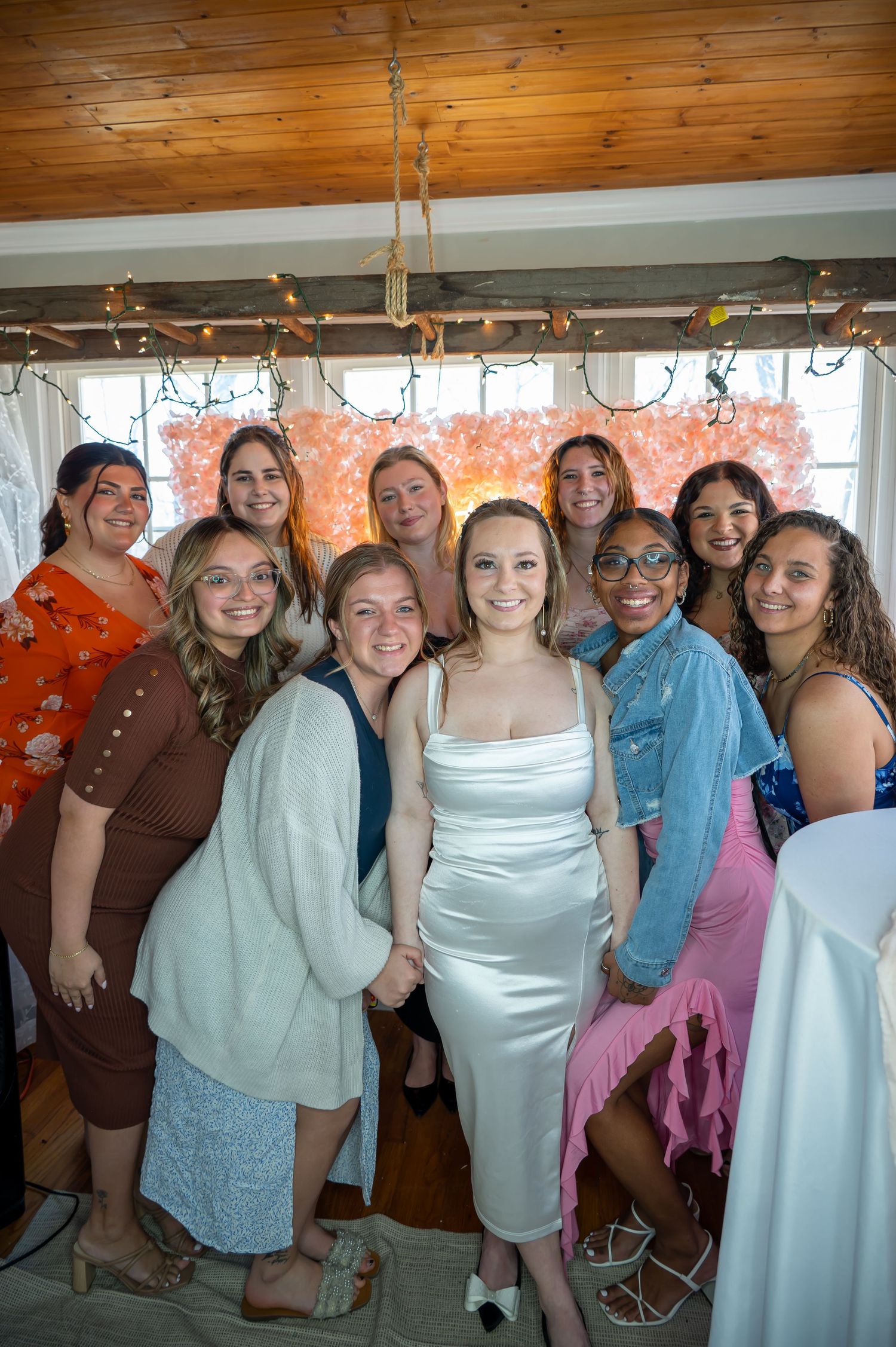 A group photo of friends in pastel-colored dresses posing together in a wood-paneled room.